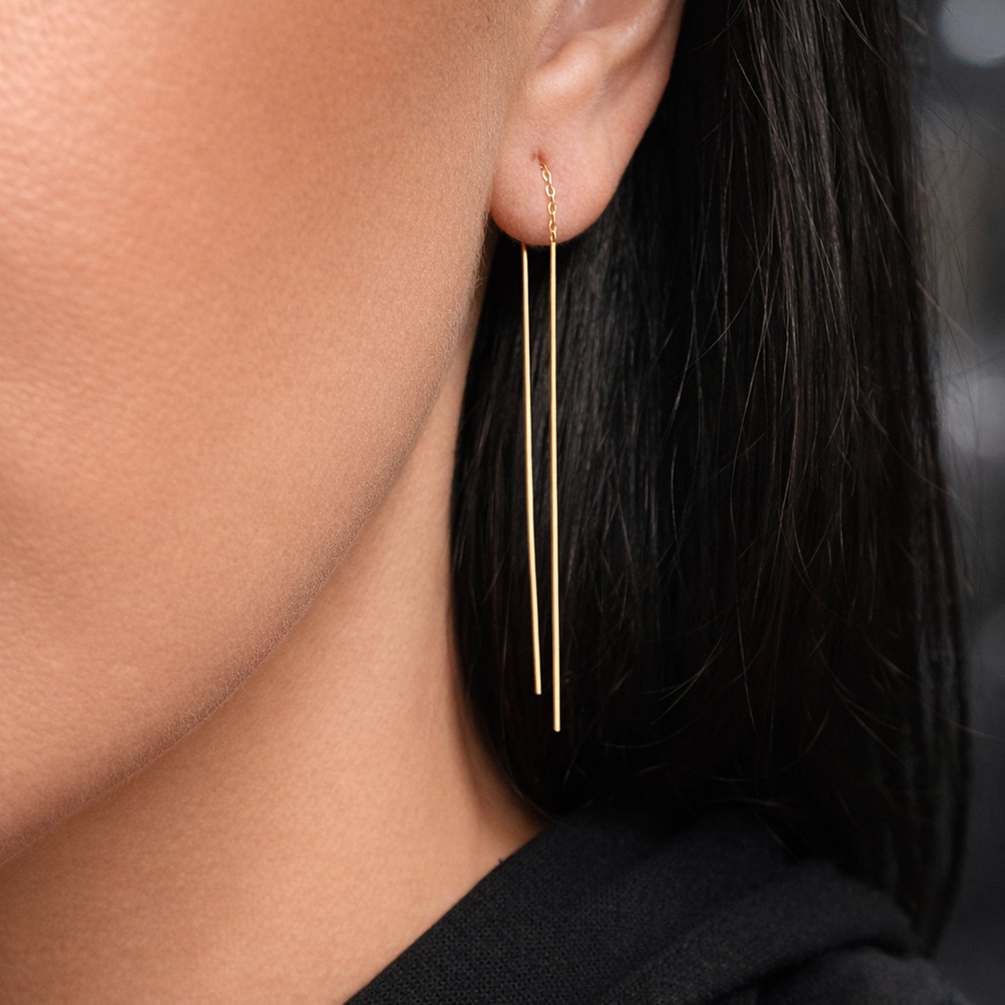 Gold minimalist double bar threader earring in polished yellow gold, featuring two slim vertical drop bars attached to a delicate chain, worn on a model with straight dark hair and smooth skin, close-up studio portrait with soft professional lighting.