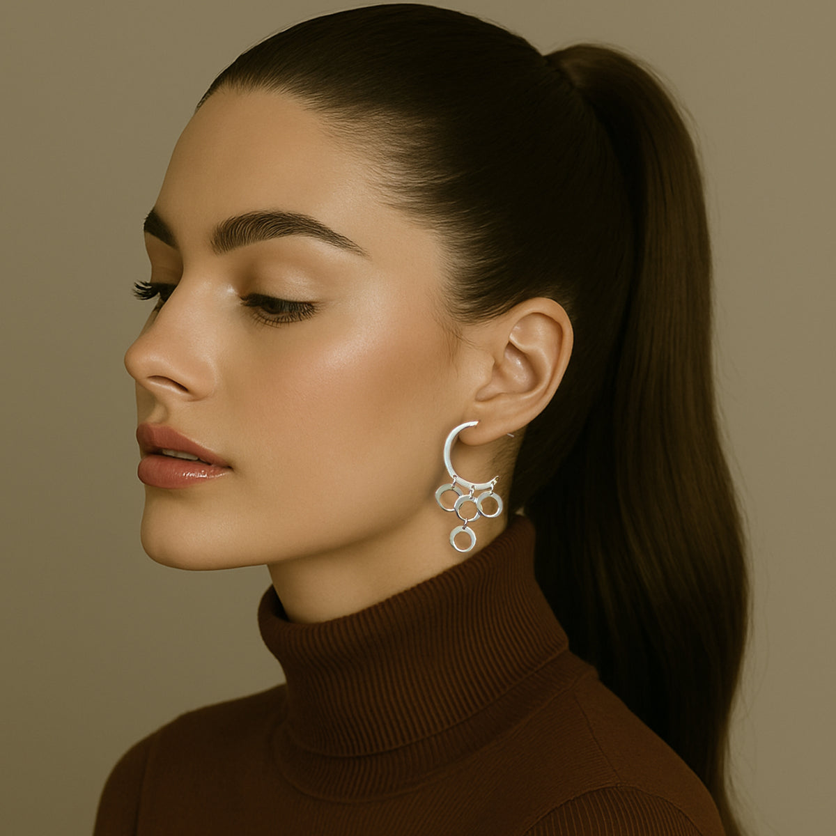 Elegant woman in a brown turtleneck with sleek ponytail wearing statement sterling silver dangle earrings featuring multiple interlinked circle drops.