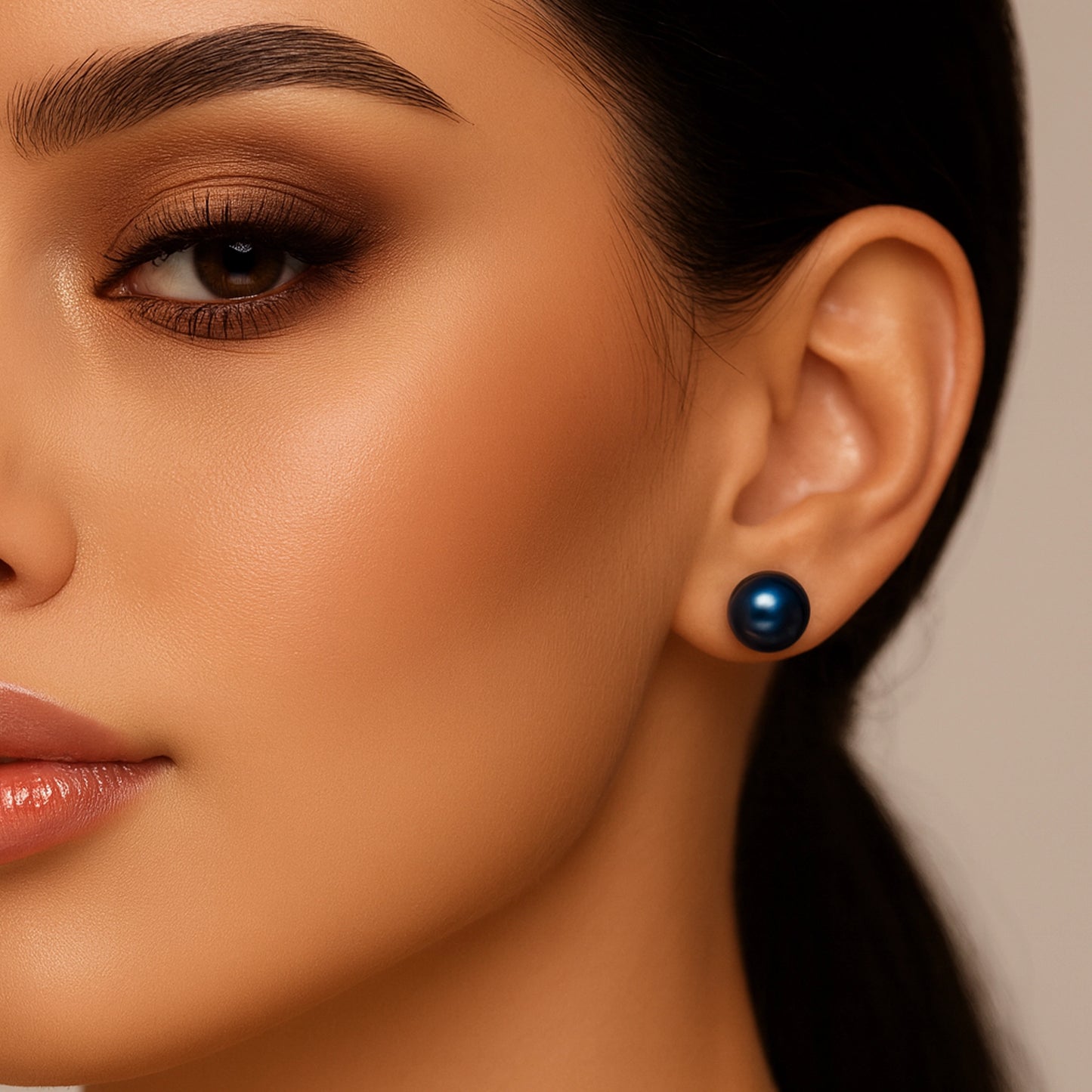 Close-up of a woman’s ear wearing a deep navy blue freshwater pearl stud earring with a subtle metallic sheen, styled with sleek black hair and soft bronze makeup.