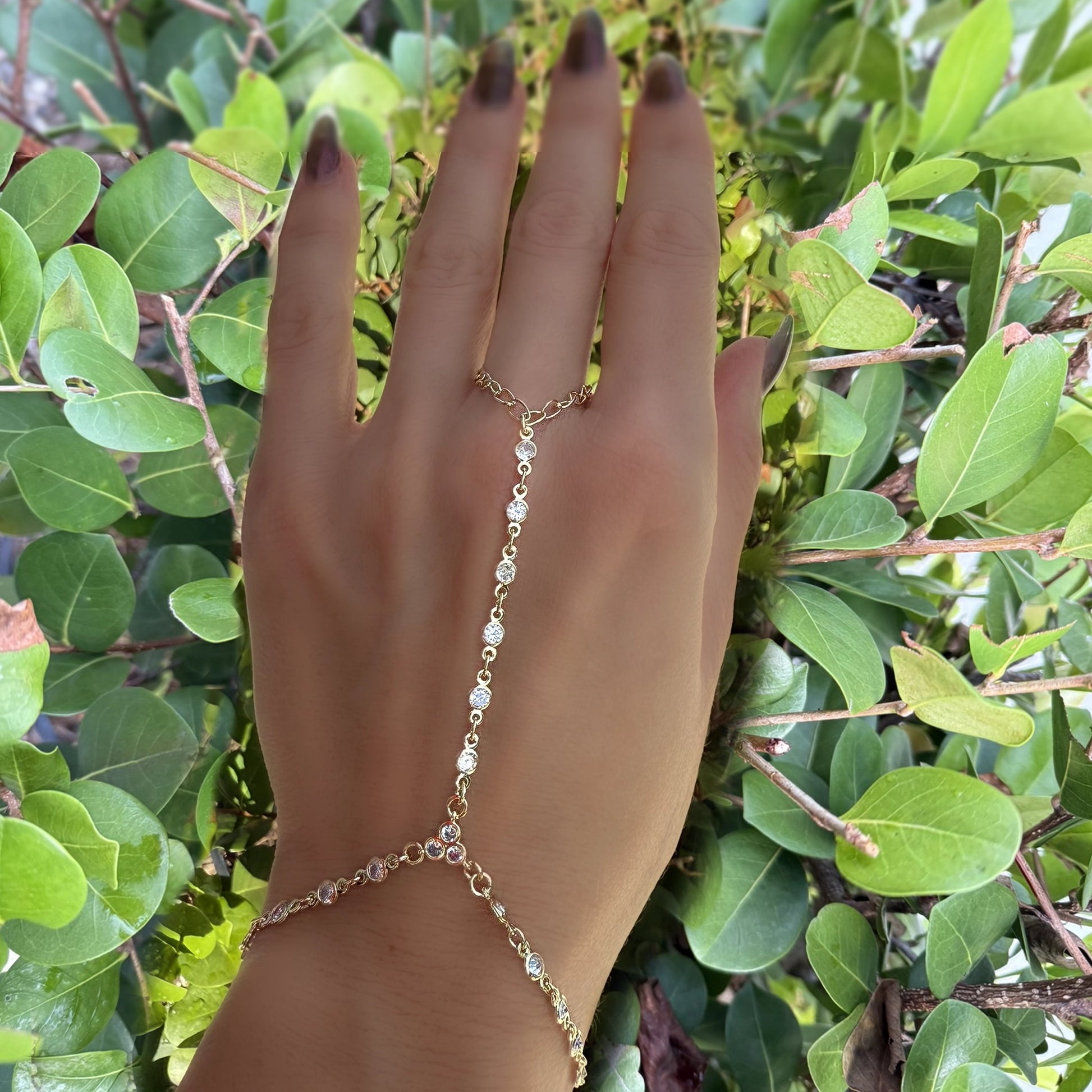 Delicate gold filled hand chain bracelet with bezel-set CZ stones, worn on hand with greenery background for a natural aesthetic.
