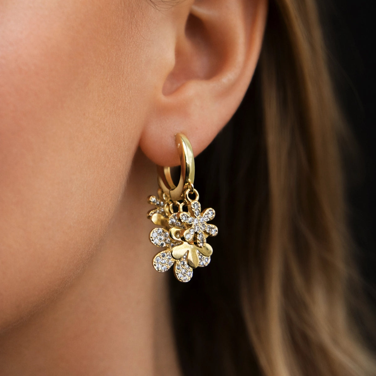 Gold filled huggie hoop earring with multiflower CZ charms, featuring sparkling cubic zirconia flower drops on a polished gold hoop, worn on ear in close-up with natural skin tones and soft studio lighting, elegant floral dangle jewelry for everyday glam or special occasions.
