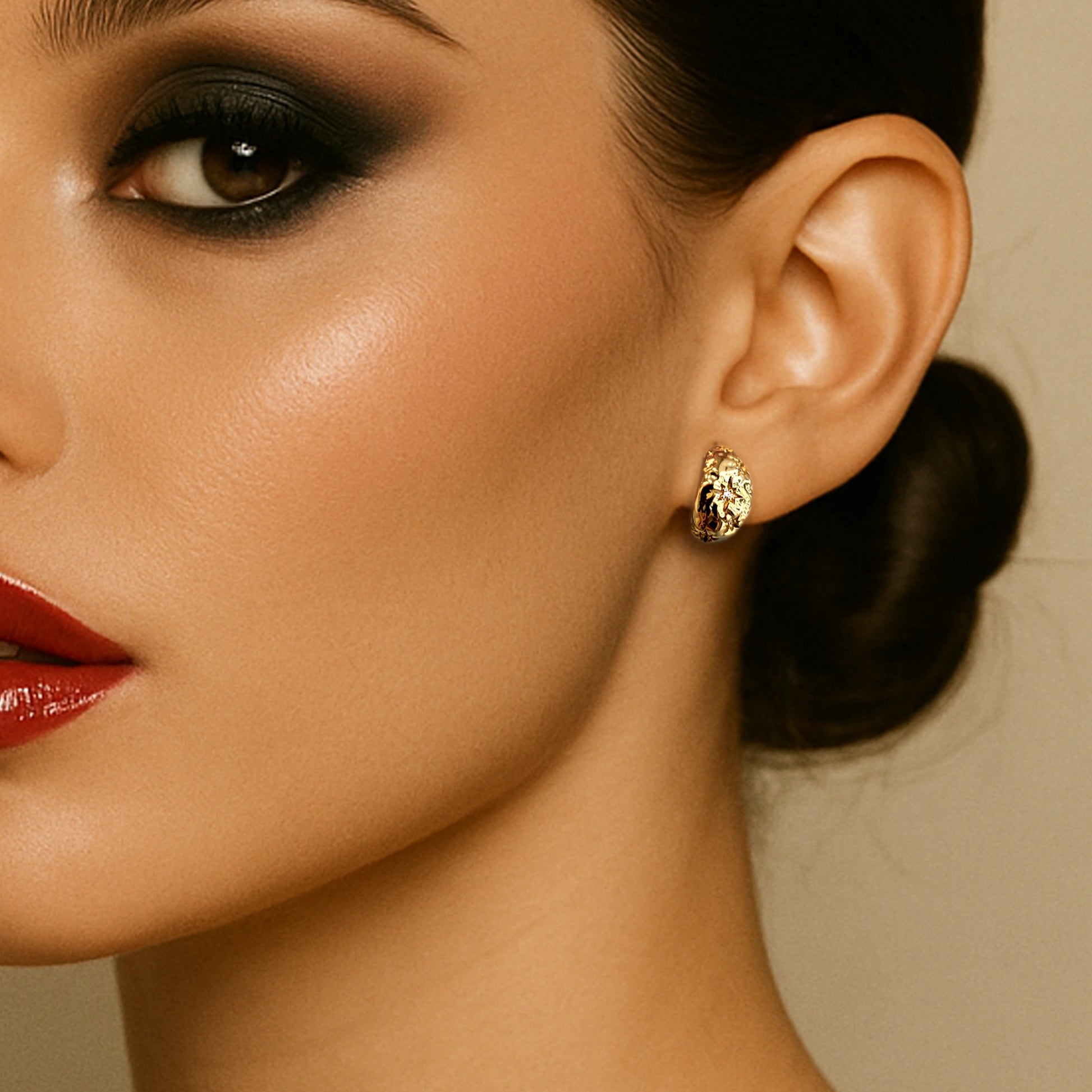 Close-up of a woman wearing bold red lipstick and a low bun, showcasing a textured gold-plated puffed moon earring against a neutral background.