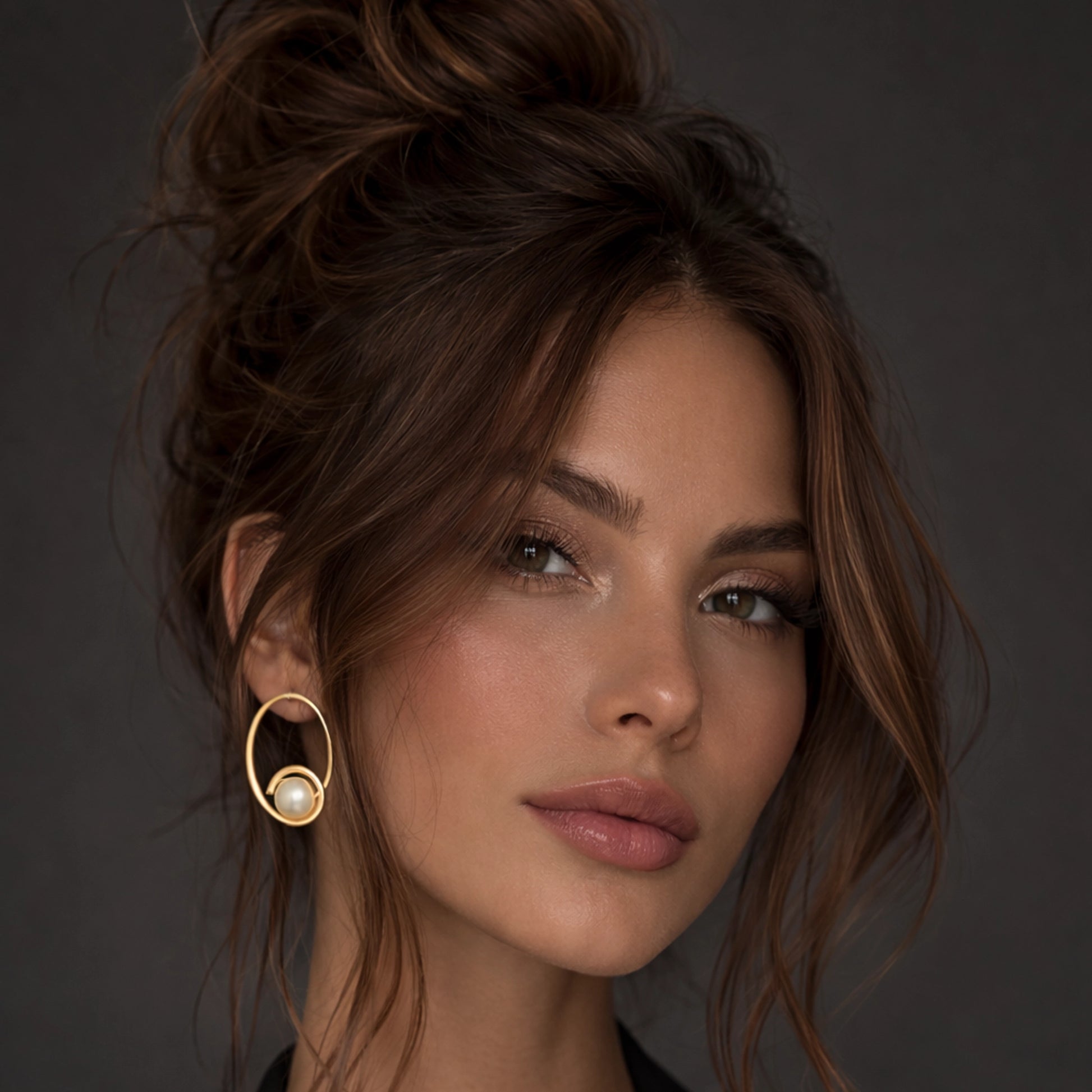 Gold hoop pearl earrings on a stylish brunette model with an elegant updo hairstyle, wearing a black blazer, close-up studio portrait with soft professional lighting, showcasing modern minimalist gold circle earrings with a single pearl accent.
