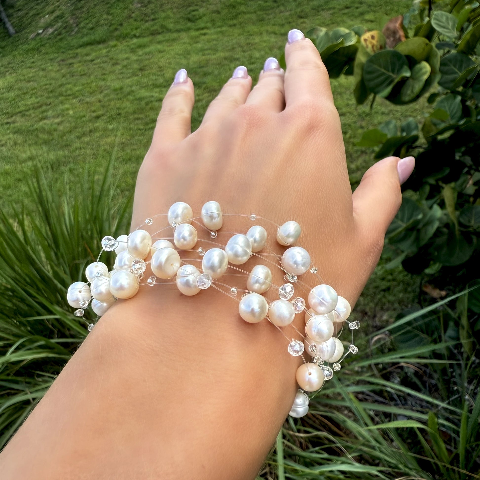 Natural white pearl and crystal bracelet styled on a wrist with a soft green garden background.