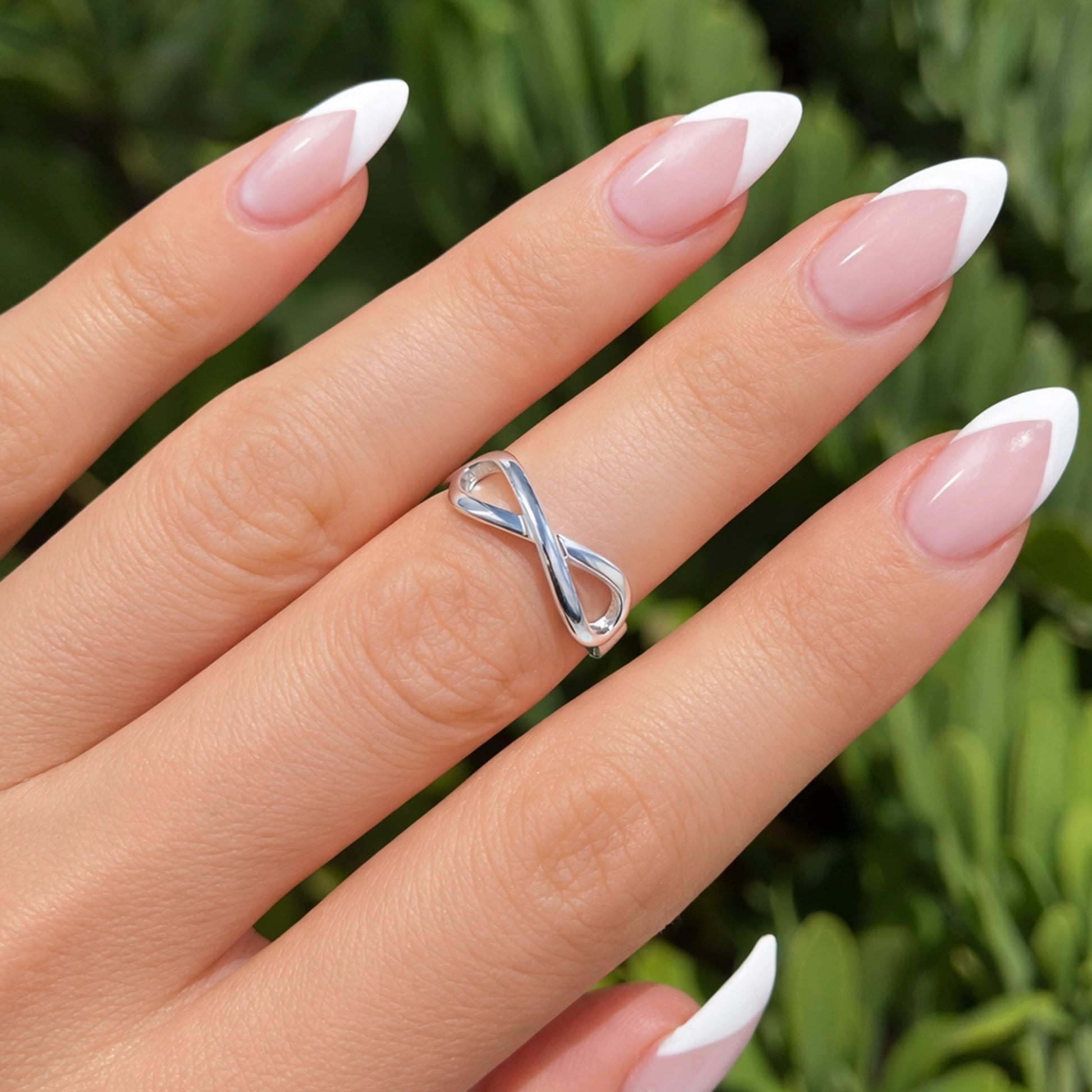 Hand wearing a silver infinity ring with a blurred green background