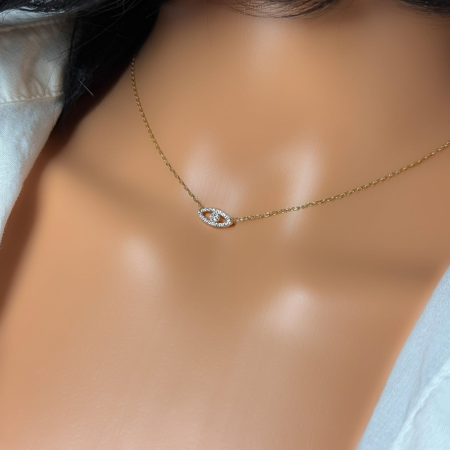 Minimalist sterling silver evil eye necklace with CZ stones in gold tone, shown on a mannequin with an open white shirt, detailed view of the pendant.