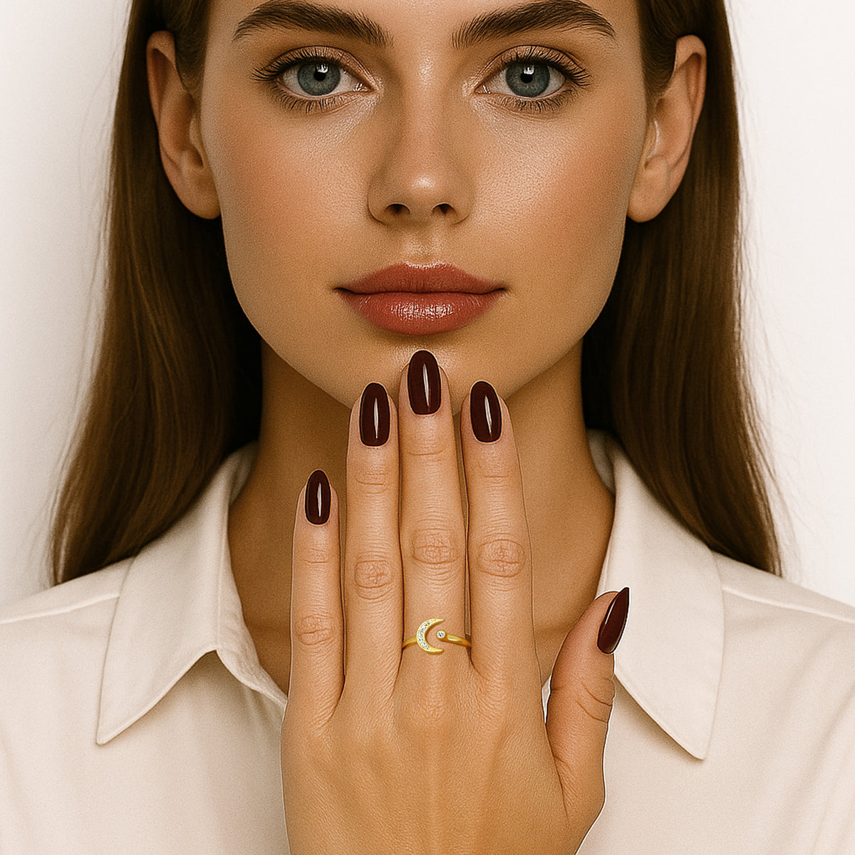 Elegant model with long brunette hair and glossy burgundy nails showcasing a gold crescent moon and star adjustable ring with CZ accents. She wears a cream blouse and holds her hand gracefully in front of her face, highlighting the celestial ring design.