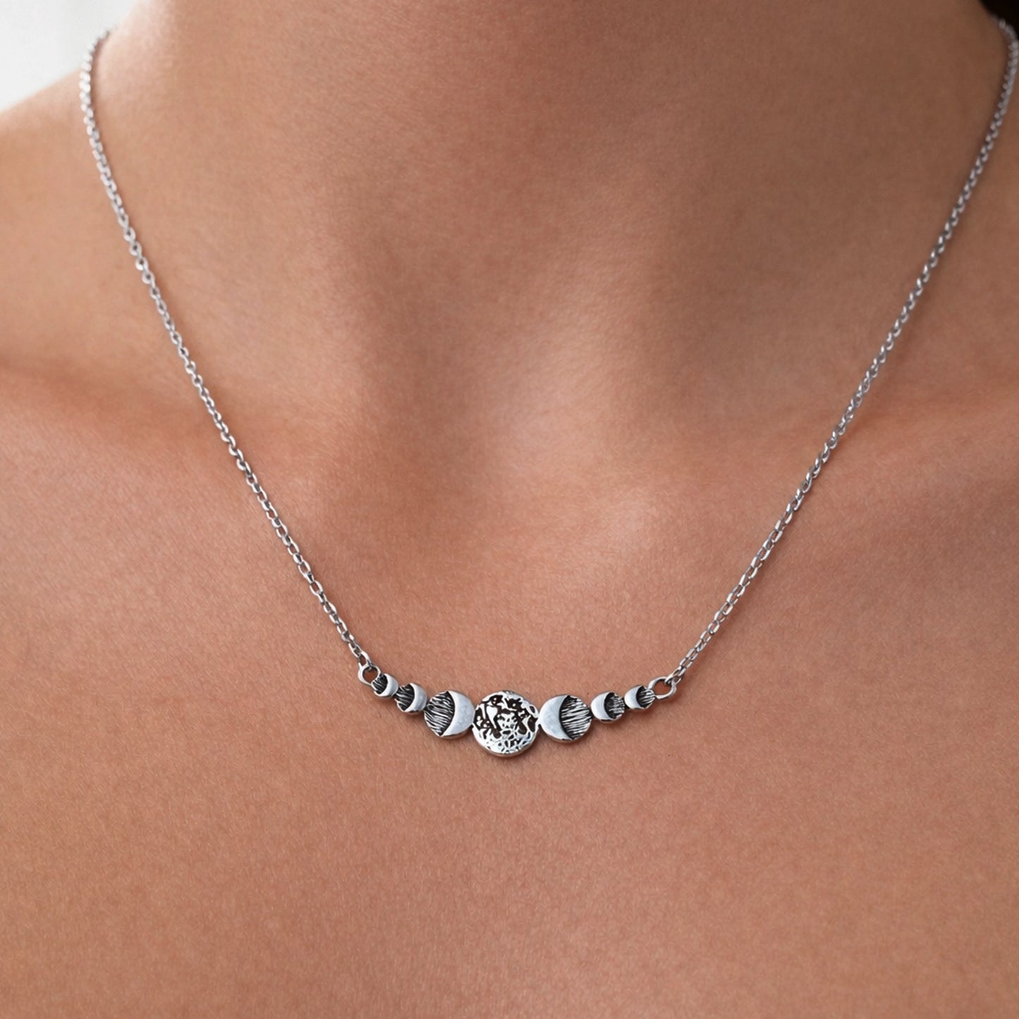 delicate silver moon-phase necklace with a central textured lunar bar, natural skin texture, soft professional lighting.