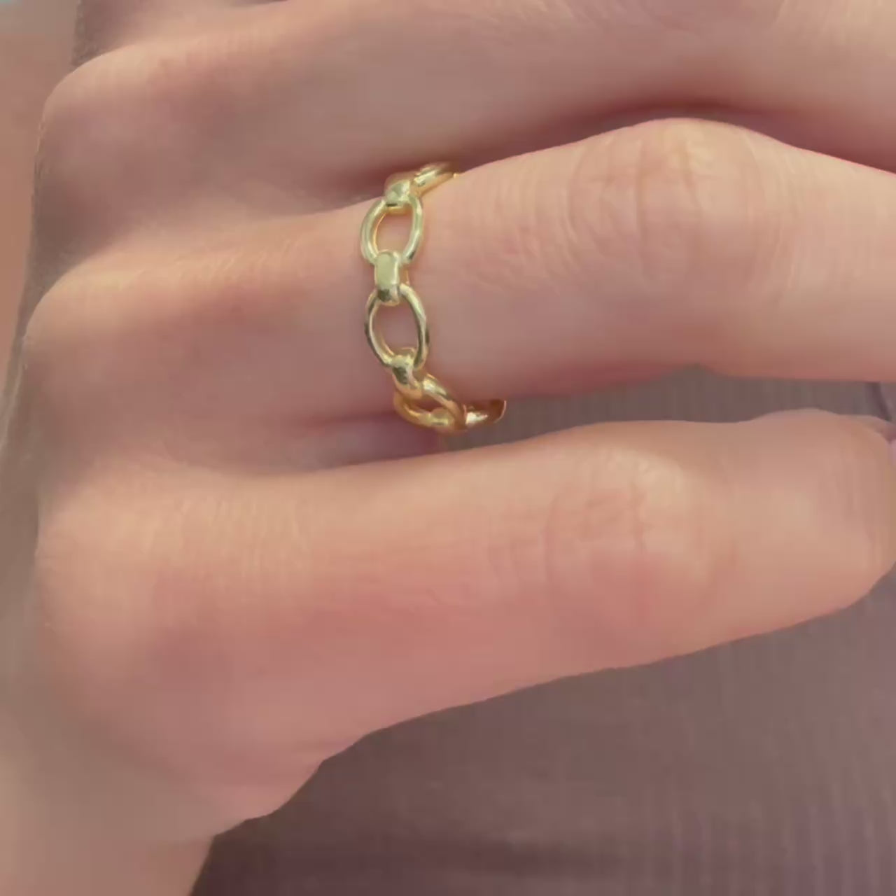 Video showcasing a trendy gold chain link ring worn on the hand, highlighting its open adjustable band and polished finish. The camera slowly moves to capture the reflective shine and interlocking links from multiple angles.