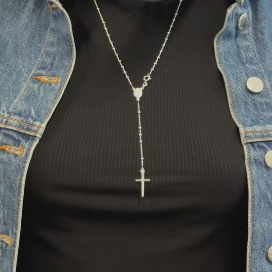 Video showing a sterling silver rosary bead necklace with a Virgin Mary centerpiece and a dangling cross pendant. The necklace is worn over a black ribbed top and styled with a denim jacket, capturing the sparkle and elegant movement of the beads and cross.