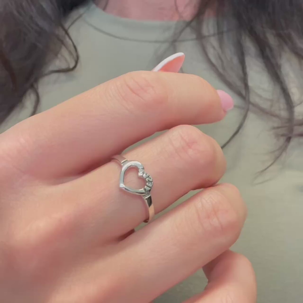 A close-up video showcasing a sterling silver ring with an open heart design engraved with the name “Jesus.” The ring is worn on a woman's hand and shown from different angles to highlight its polished finish, minimalist design, and faith-inspired symbolism.