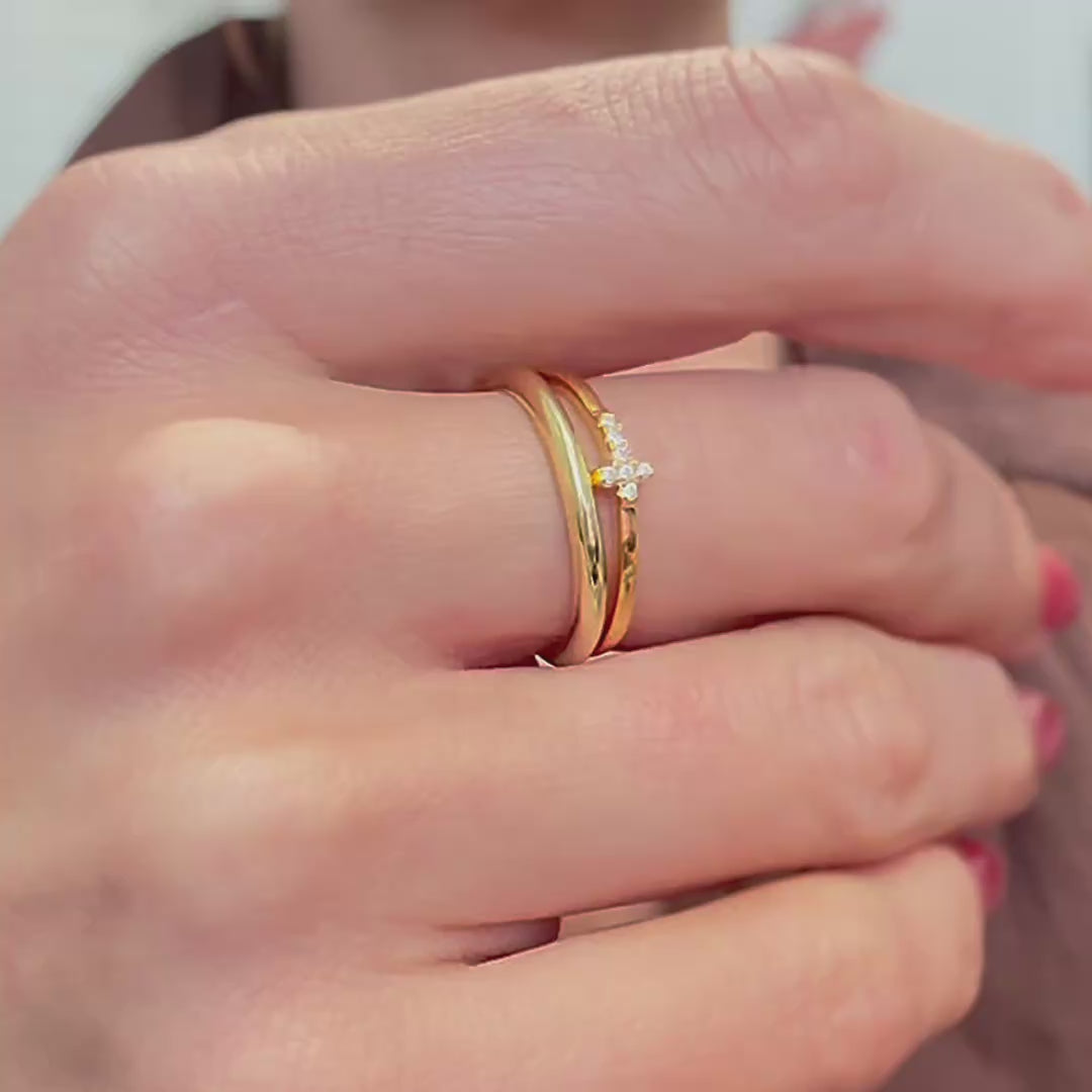 Rotating view of a dainty sterling silver ring set plated in gold, featuring a sideways cubic zirconia cross on the top ring, shown on a woman's finger.