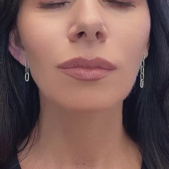 Video showcasing mismatched sterling silver chain link drop earrings with cubic zirconia accents. The earrings dangle elegantly from the model’s ears, catching the light with every movement against a clean white background.