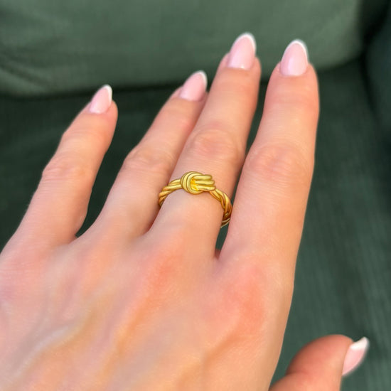 Sterling silver love knot ring with gold plating, showcased on a model's hand in natural lighting. The ring features a twisted rope design and is highlighted with close-up movement to capture shine and detail.
