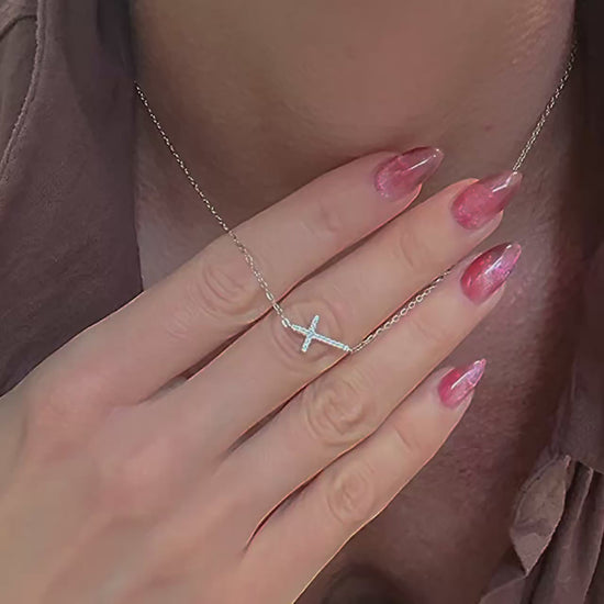 A dainty sterling silver necklace featuring a sideways CZ cross pendant, gently resting on the mannequin’s neckline. The camera pans to show the fine chain and sparkling cubic zirconia details, styled with a soft white shirt.