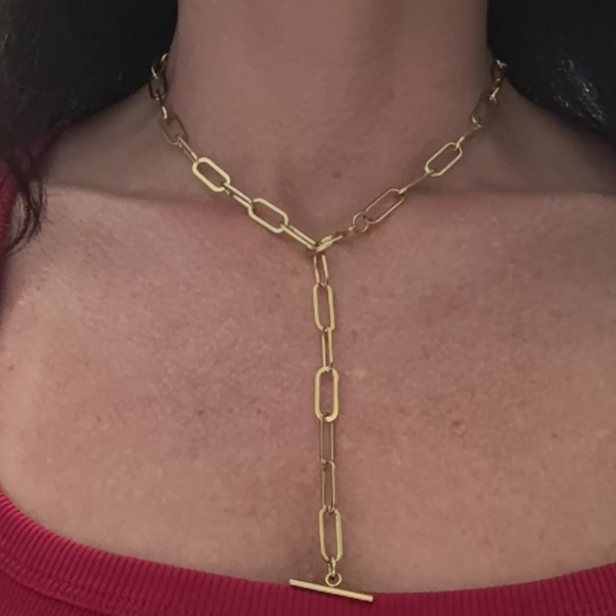 Close-up video of a gold paperclip chain necklace with a toggle clasp, made from stainless steel and plated in 18K gold. The necklace is shown from multiple angles, highlighting its lariat-style versatility, polished finish, and bold link design.