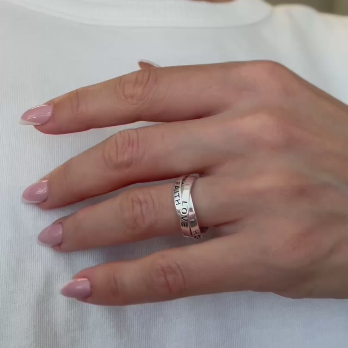 Rotating close-up video of a sterling silver triple-band ring engraved with "FAITH", "LOVE", and "HOPE" on a woman's hand with glossy French manicure.