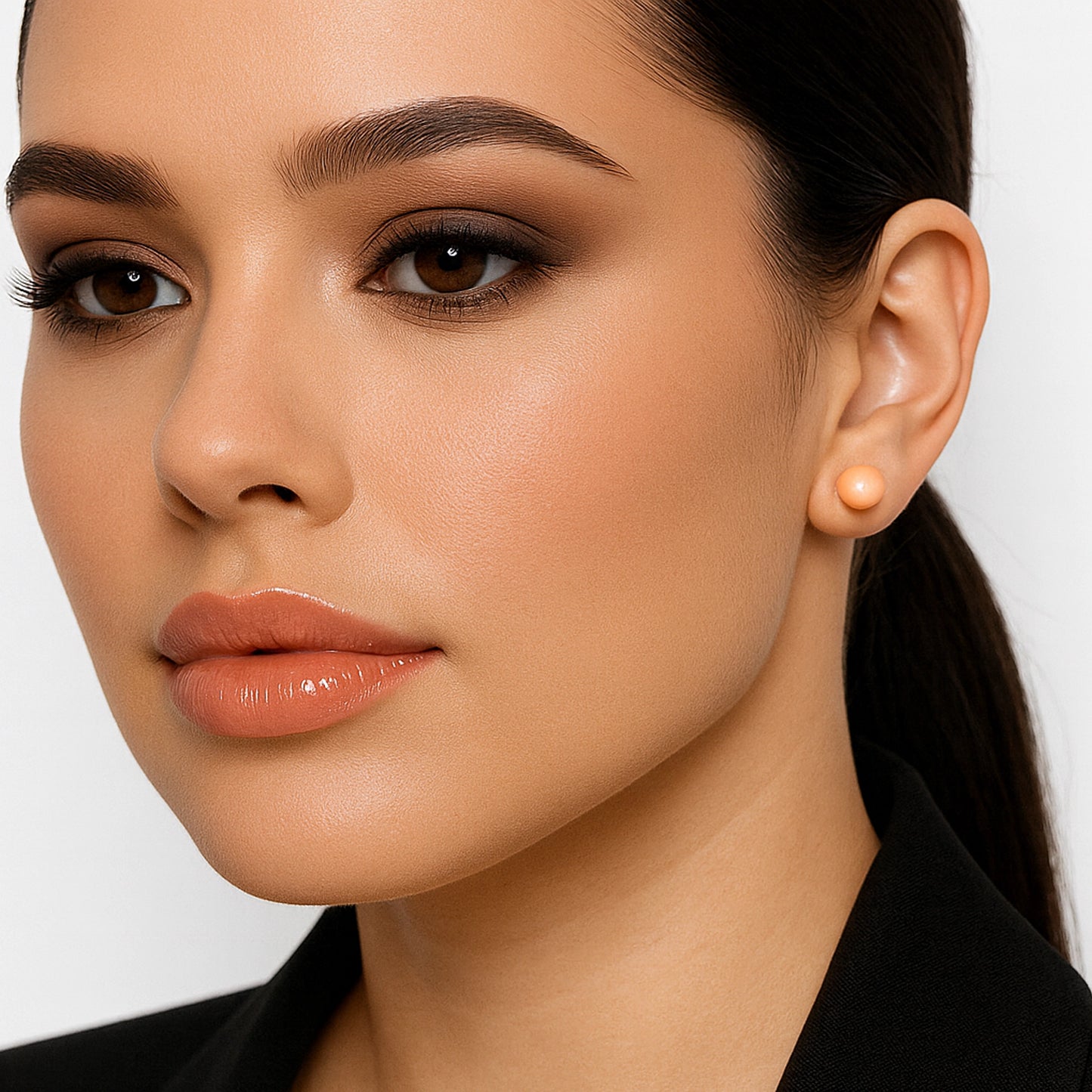 Elegant woman wearing a peach freshwater pearl earring on her left ear, styled with a sleek ponytail and warm-toned makeup for a sophisticated look.