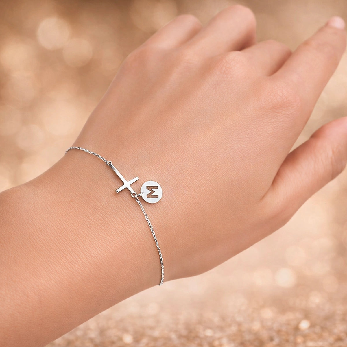 Sterling silver cross charm bracelet with personalized initial disc on delicate chain, minimalist religious jewelry on woman’s wrist, dainty Christian bracelet gift for her, elegant everyday faith jewelry in silver.