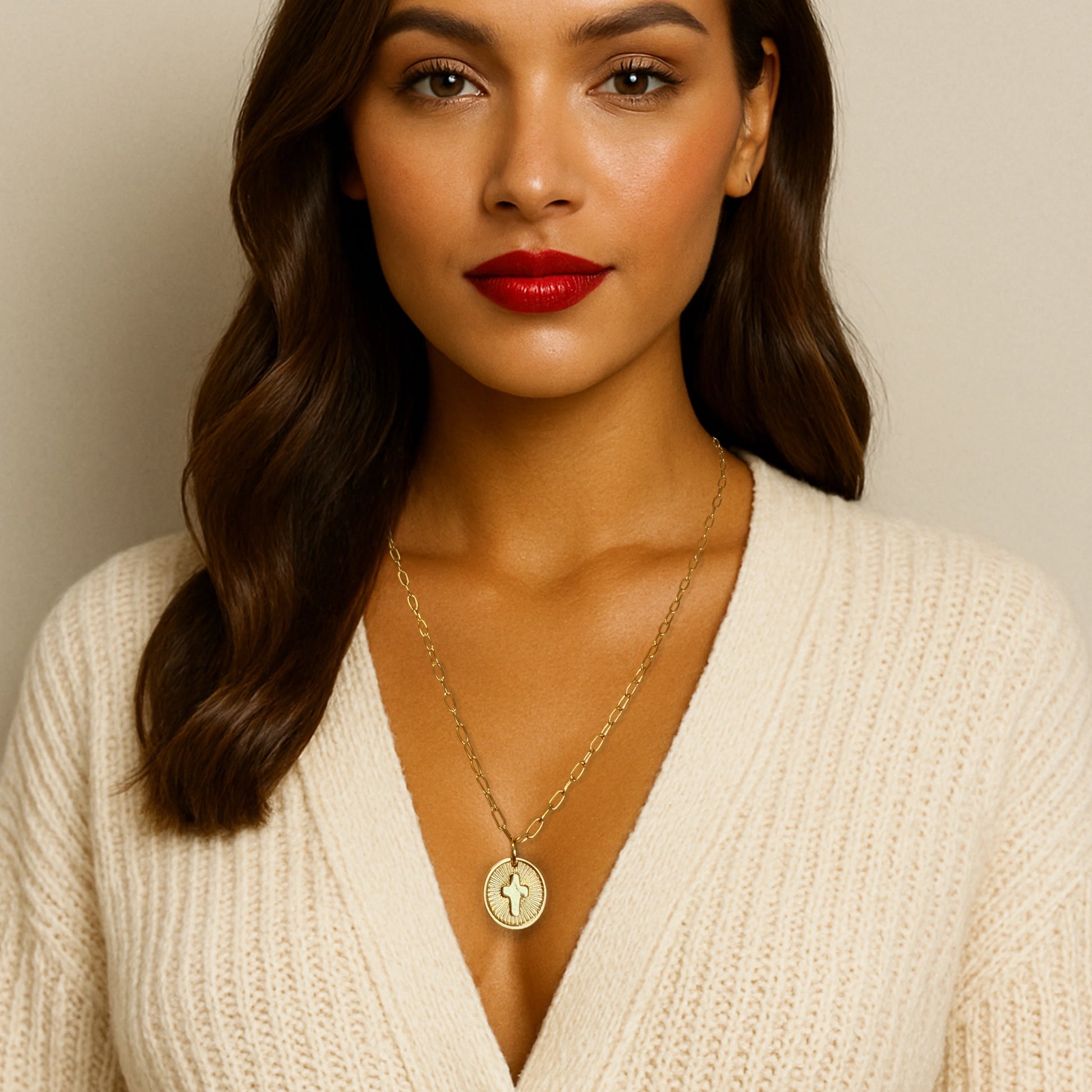 Woman wearing a statement cross medallion necklace in 18k gold filled, styled with a cream sweater, showcasing the necklace's length and elegant sunburst design.