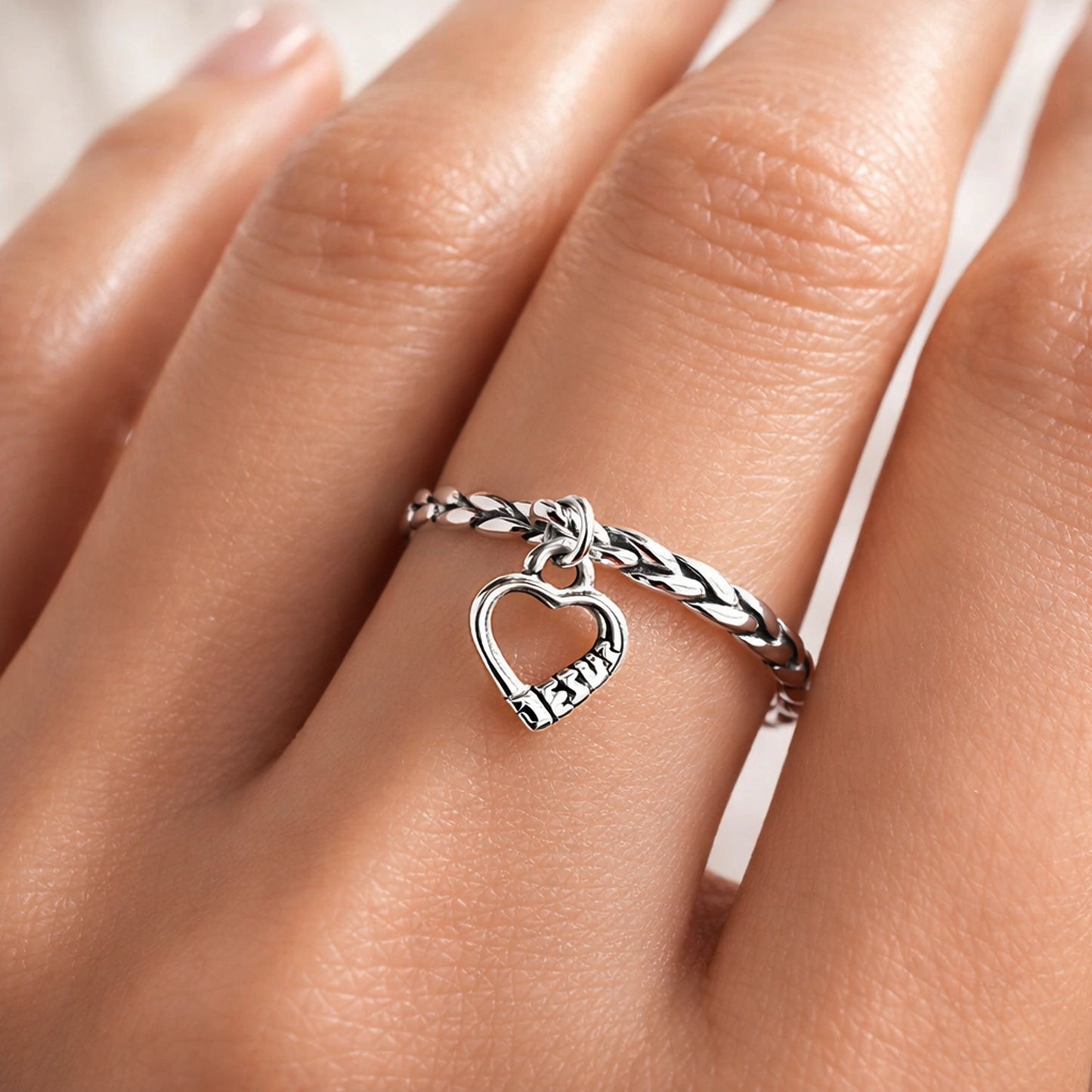 Outdoor shot of a silver heart Jesus ring on the hand, with a blurred leafy background and natural sunlight.