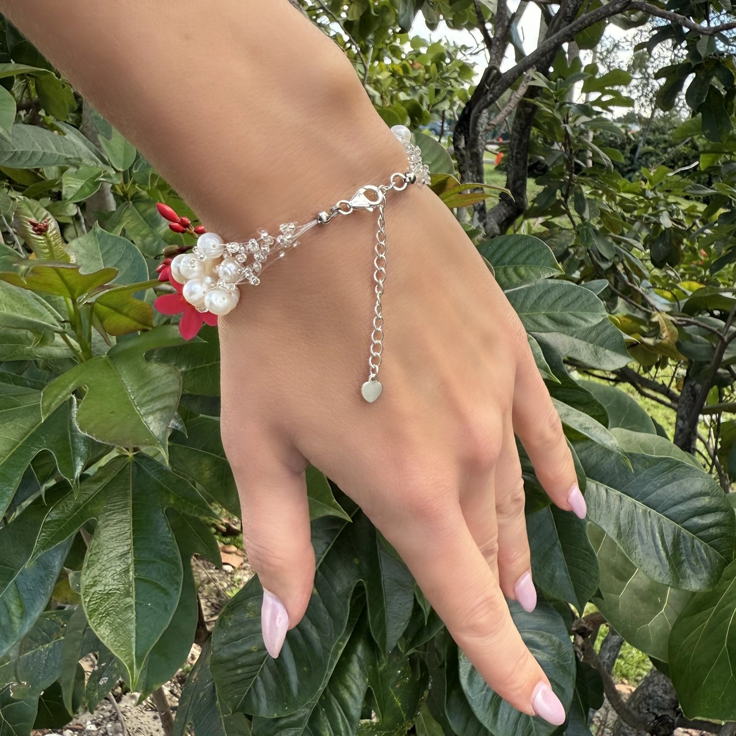 Back view of multi-strand pearl bracelet featuring an adjustable silver extender chain with heart detail, worn on a hand surrounded by leaves.
