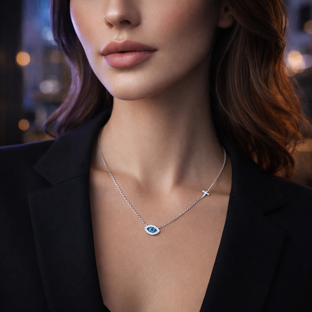 high-end product photo of a modern model wearing a black blazer with sleek contemporary makeup and softly styled hair. A silver evil eye necklace with a vivid blue center stone and a small side cross is clearly visible. Professional studio lighting, soft blurred background, sharp focus on the jewelry.