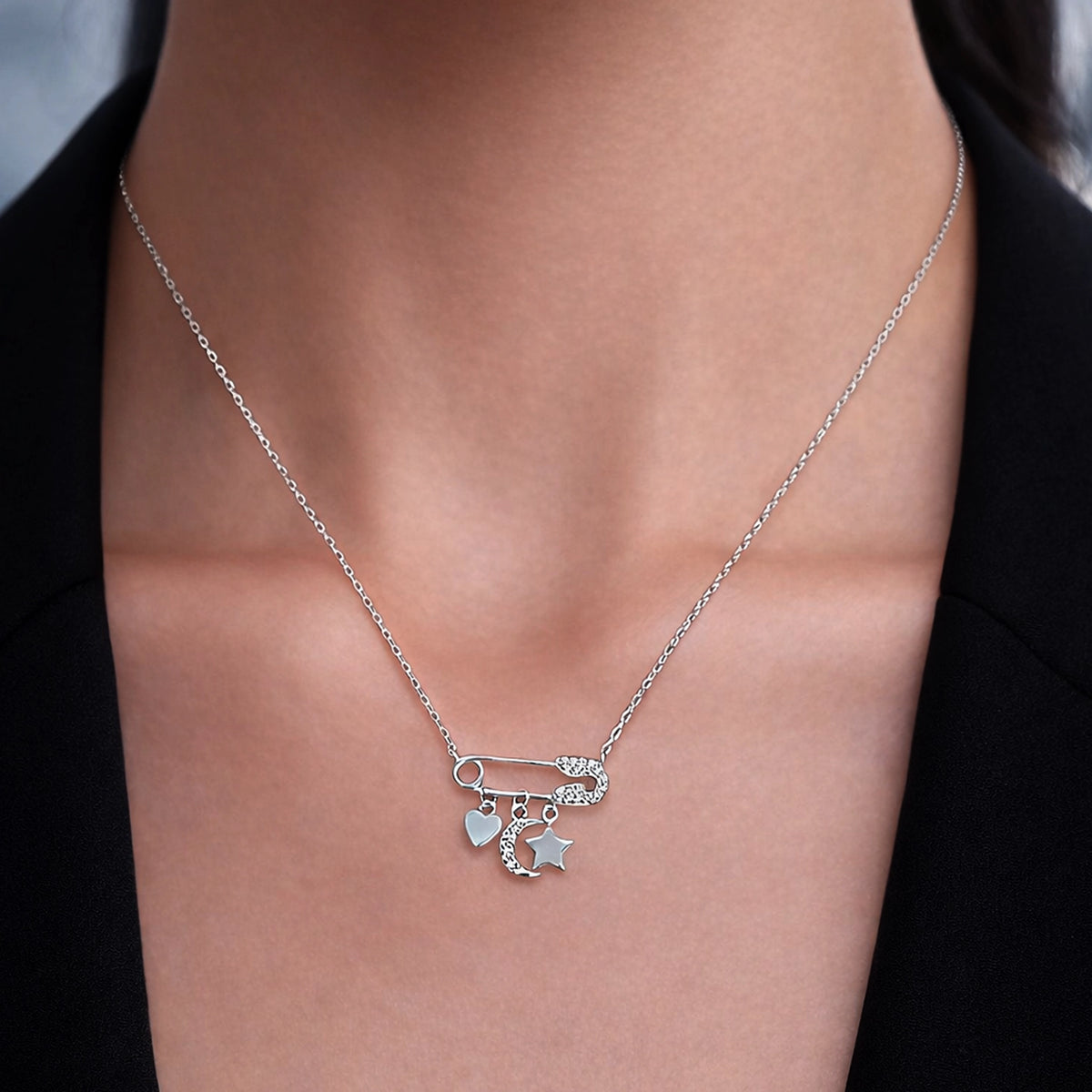 Close-up of sterling silver pin necklace featuring cubic zirconia heart, moon, and star charms.