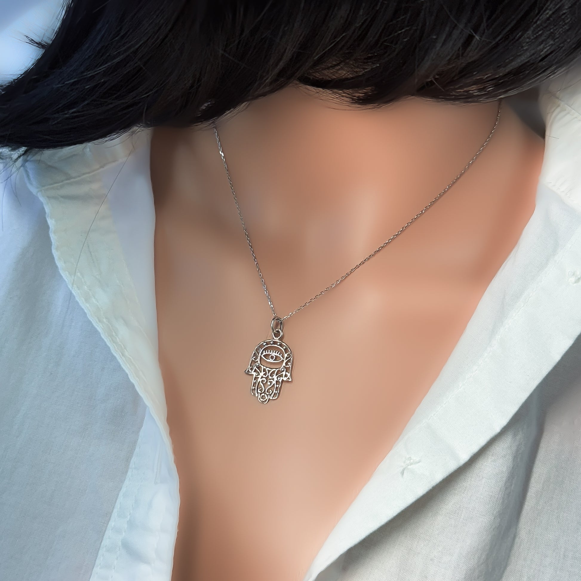 Elegant sterling silver Hamsa hand and evil eye pendant necklace showcased on a mannequin with a white shirt, highlighting the delicate spiritual design.
