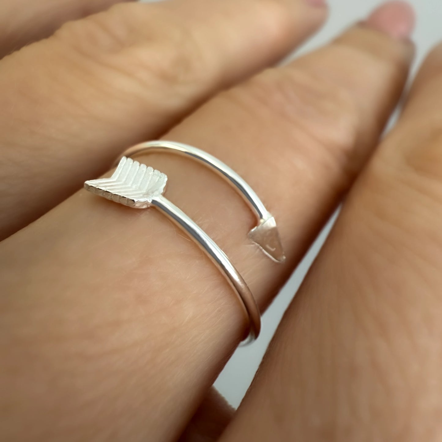 Close-up side view of a sterling silver arrow ring featuring a pointed tip and feathered fletching design, elegantly wrapping around the finger.