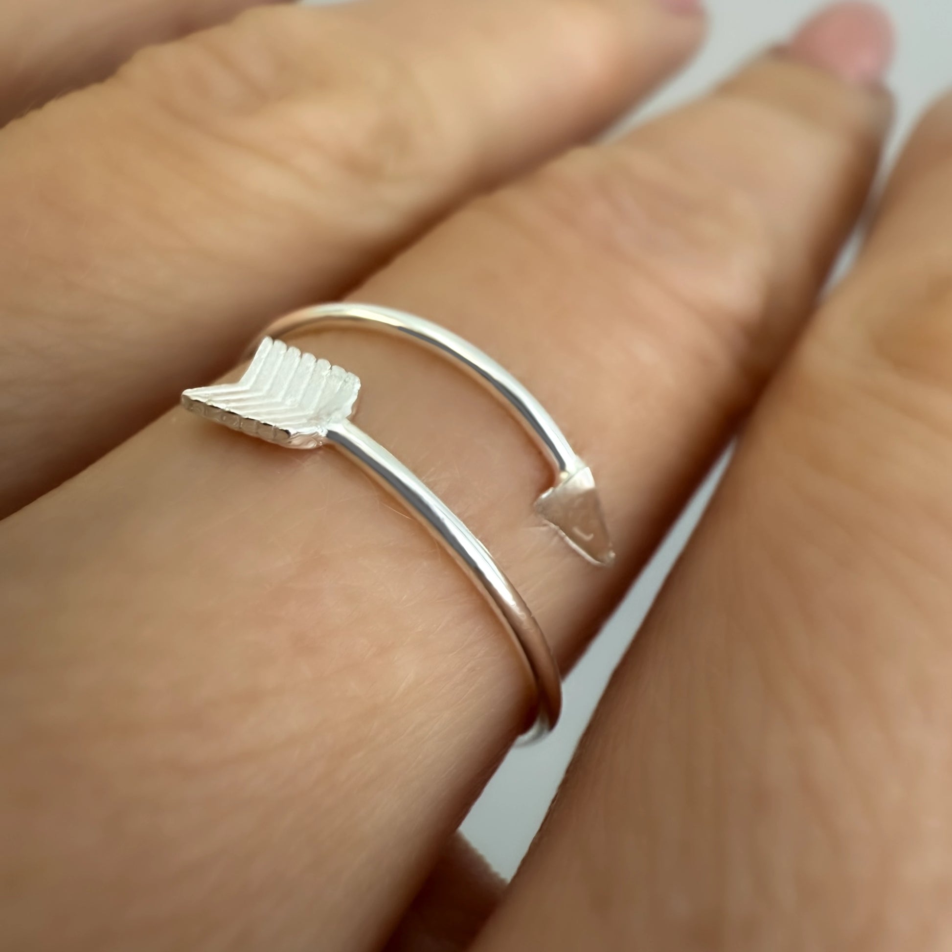 Close-up side view of a sterling silver arrow ring featuring a pointed tip and feathered fletching design, elegantly wrapping around the finger.