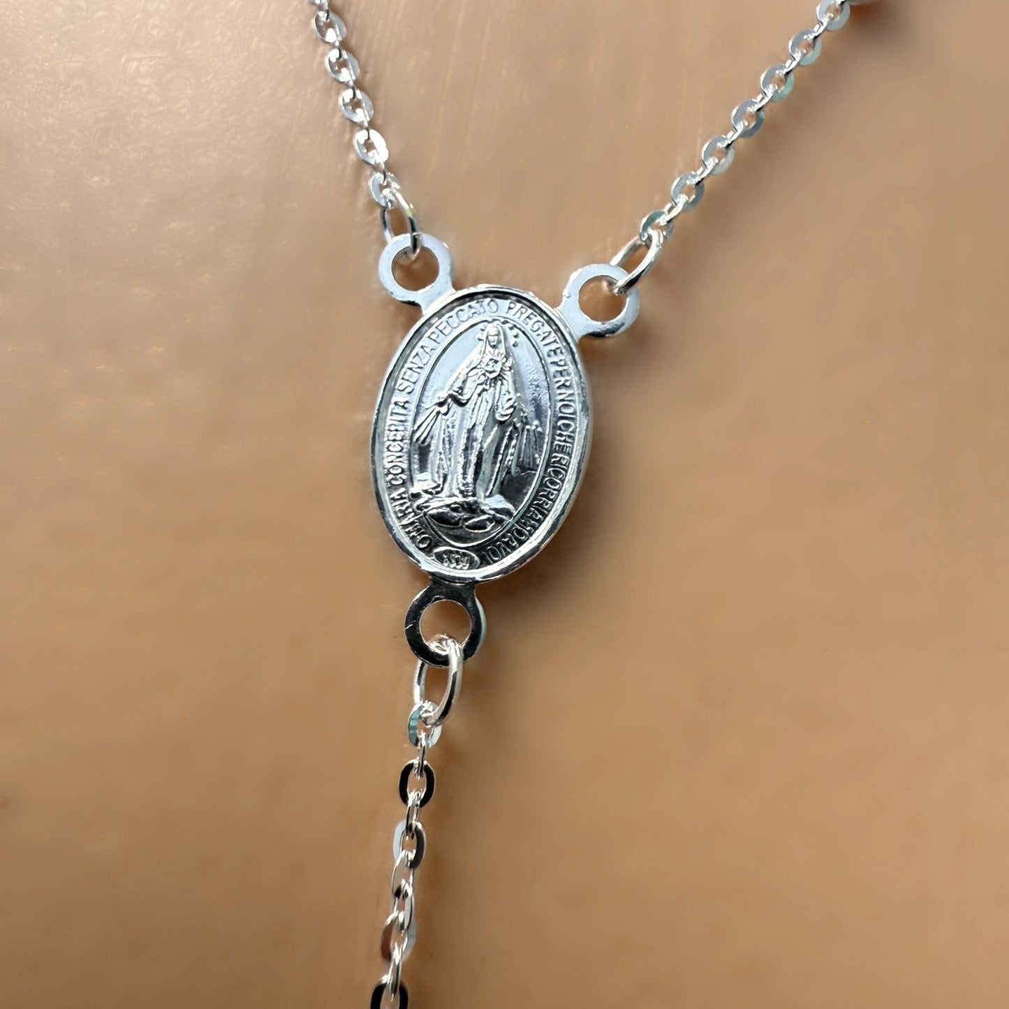 Macro close-up of the front side of a sterling silver Miraculous Medal pendant with engraved Virgin Mary figure.