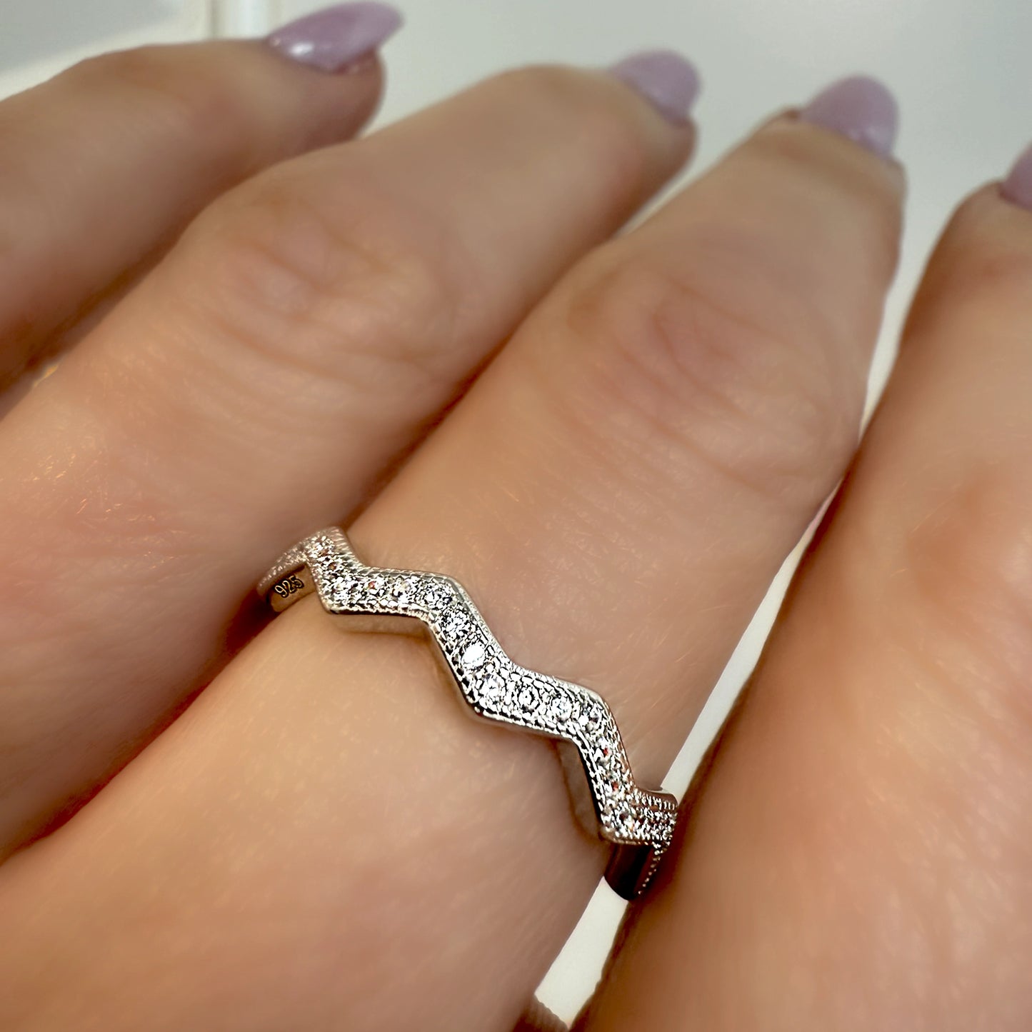A sterling silver chevron wave ring encrusted with small sparkling cubic zirconia stones, worn on a hand with soft lavender nail polish.