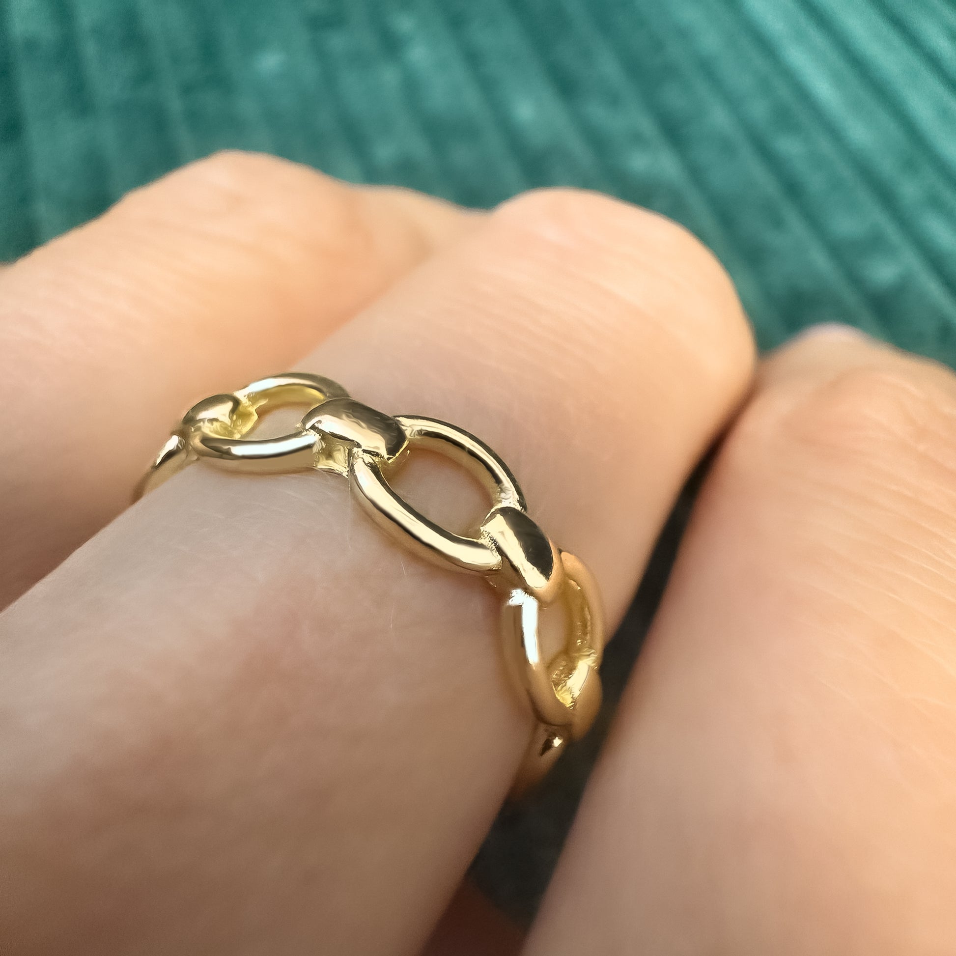 Side view of a gold link ring on finger, capturing light and detail of each rounded link in a soft natural light.