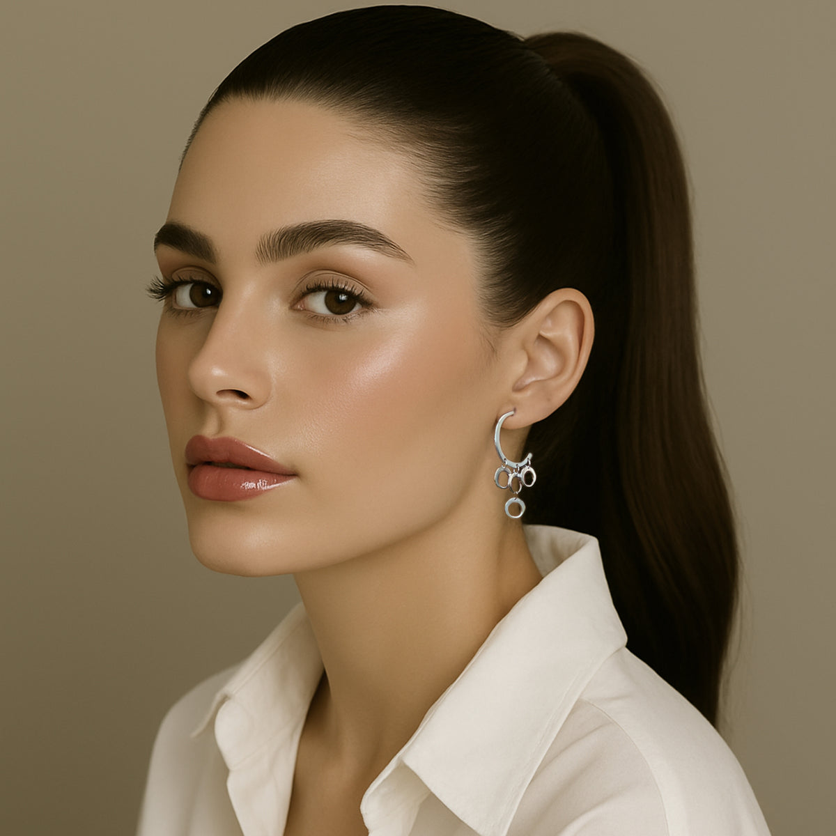 Stylish woman with sleek ponytail wearing a white collared shirt and bold sterling silver chandelier earrings with interlinked hoops in a crescent design.