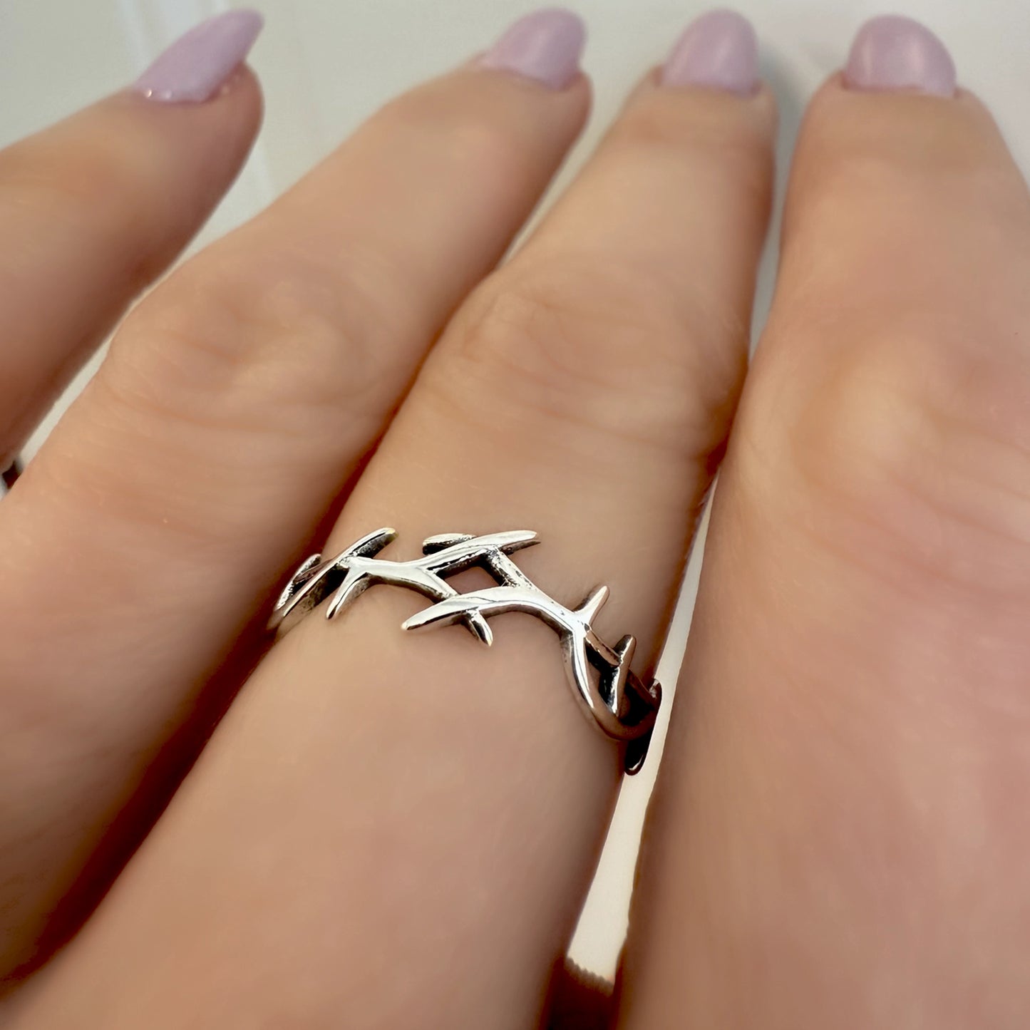 Sterling silver crown of thorns ring worn on a hand with soft lilac manicure, showcasing a delicate Christian band with thorny vine design symbolizing Jesus' sacrifice.