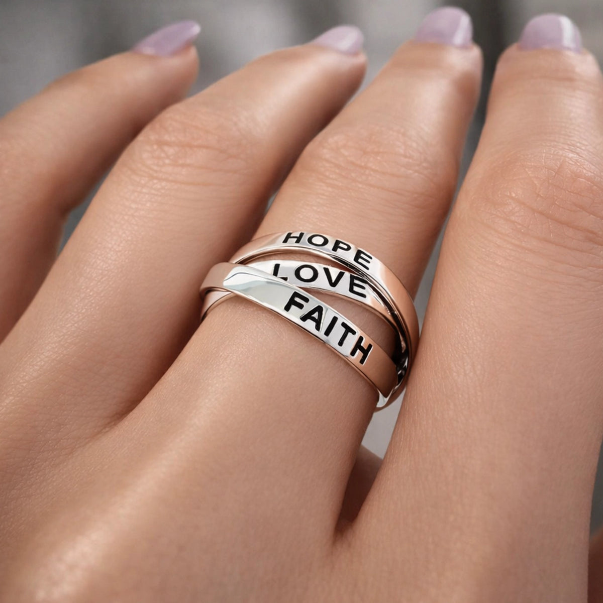 Close-up of a hand wearing a sterling silver triple band ring engraved with the words "FAITH," "LOVE," and "HOPE" on each band, stacked together.