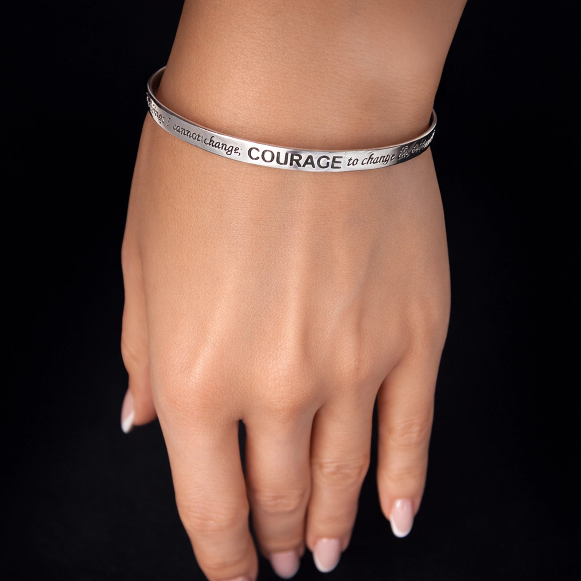 Engraved cuff silver bracelet with Serenity Prayer on elegant female wrist, polished sterling silver inspirational bracelet with “COURAGE” engraving, minimalist open cuff bracelet jewelry, high-end studio lighting, luxury motivational jewelry gift for women, close-up hand model, premium presentation, spiritual affirmation bracelet, Christian inspirational jewelry, modern silver cuff bracelet detail.