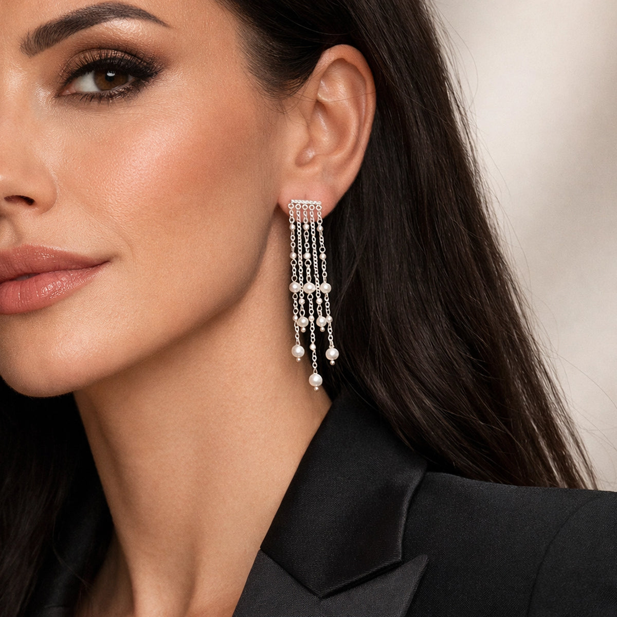 Close-up of a woman wearing long chandelier drop earrings with natural freshwater pearls and silver chain strands, styled with glossy lips and a black stylish blazer.