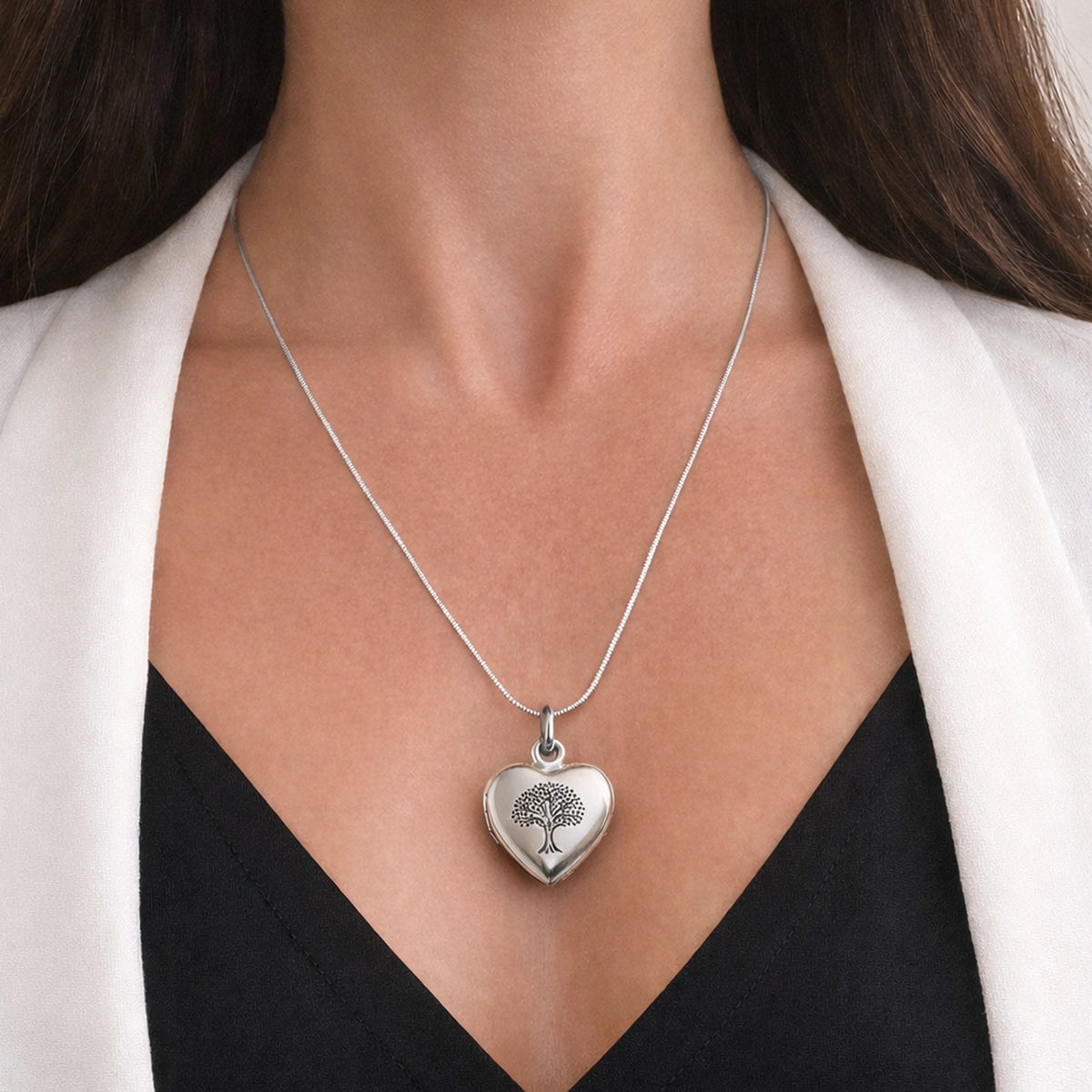 Silver heart-shaped necklace with a tree design worn by a person