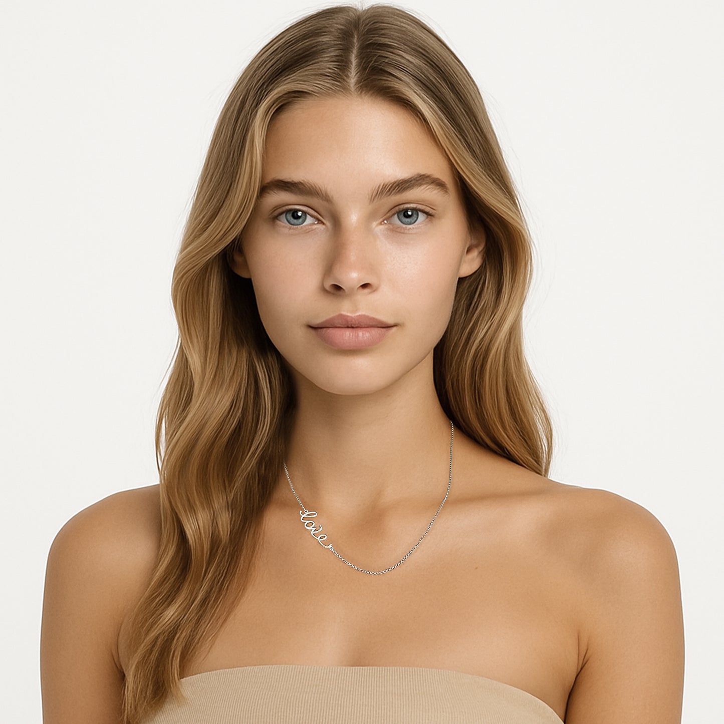 A young woman with long blonde hair wearing a sterling silver ‘love’ script necklace. She is facing forward against a white background, dressed in a nude strapless top.