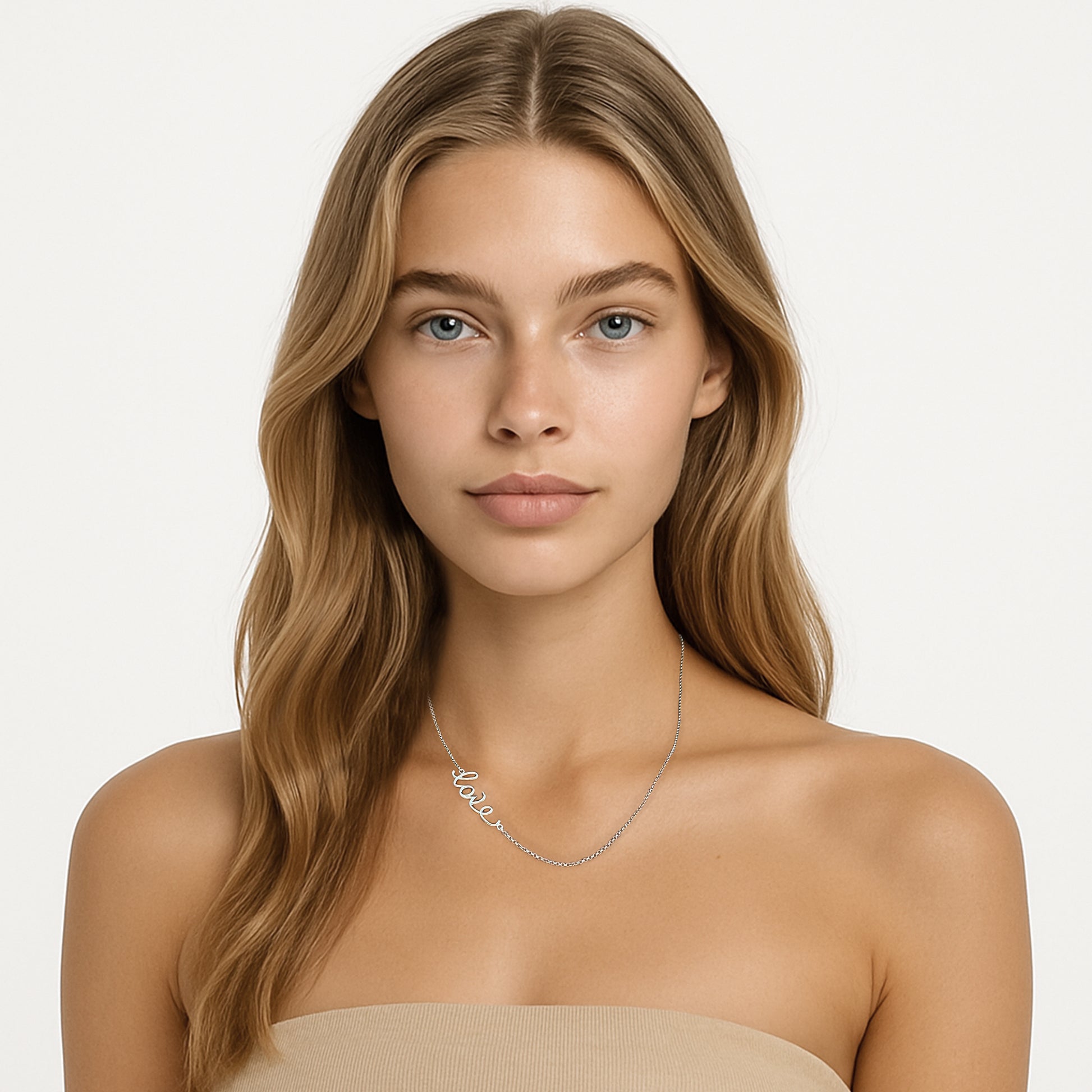 A young woman with long blonde hair wearing a sterling silver ‘love’ script necklace. She is facing forward against a white background, dressed in a nude strapless top.