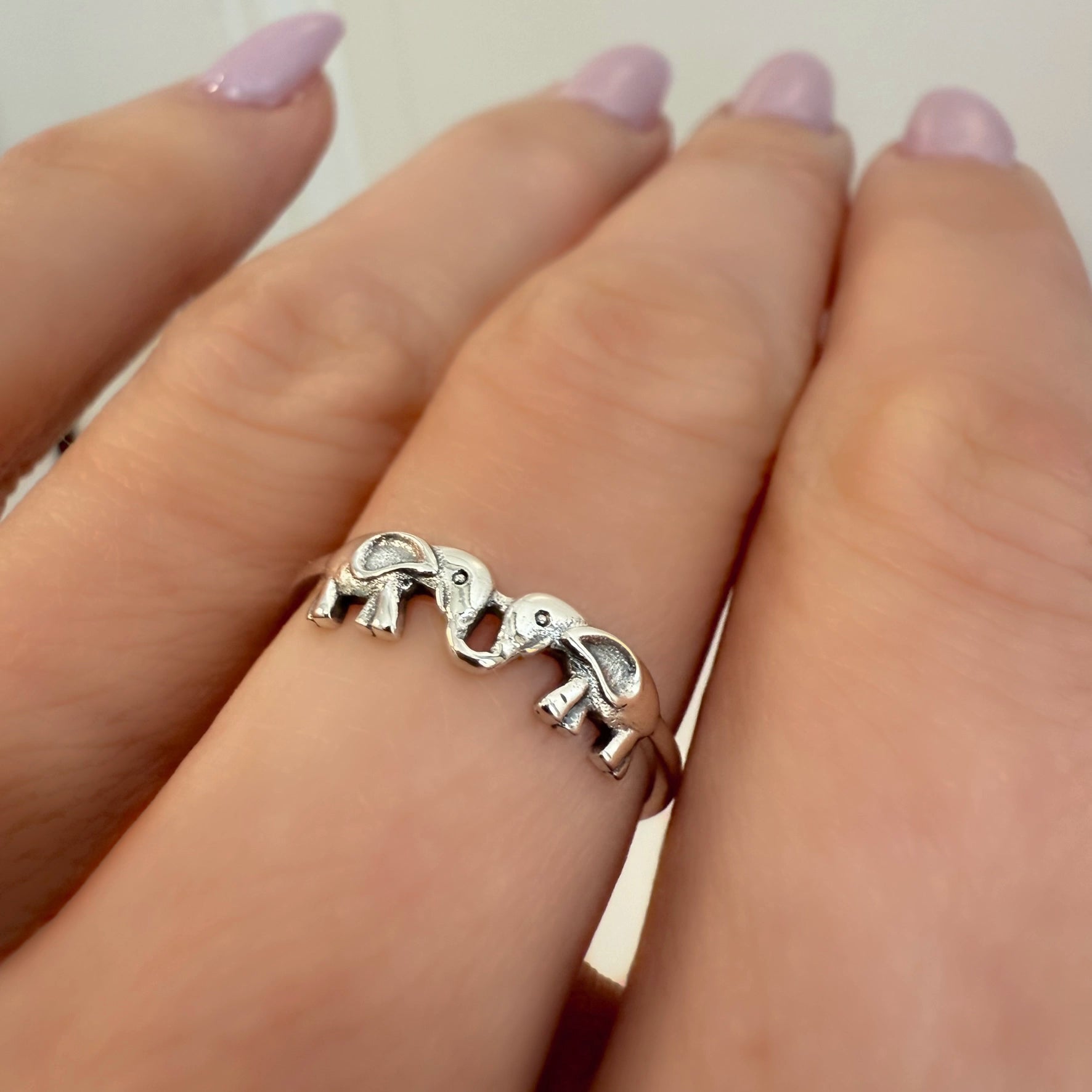 Sterling silver ring featuring two elephants touching trunks, symbolizing love and connection, worn on finger with light pink nails.
