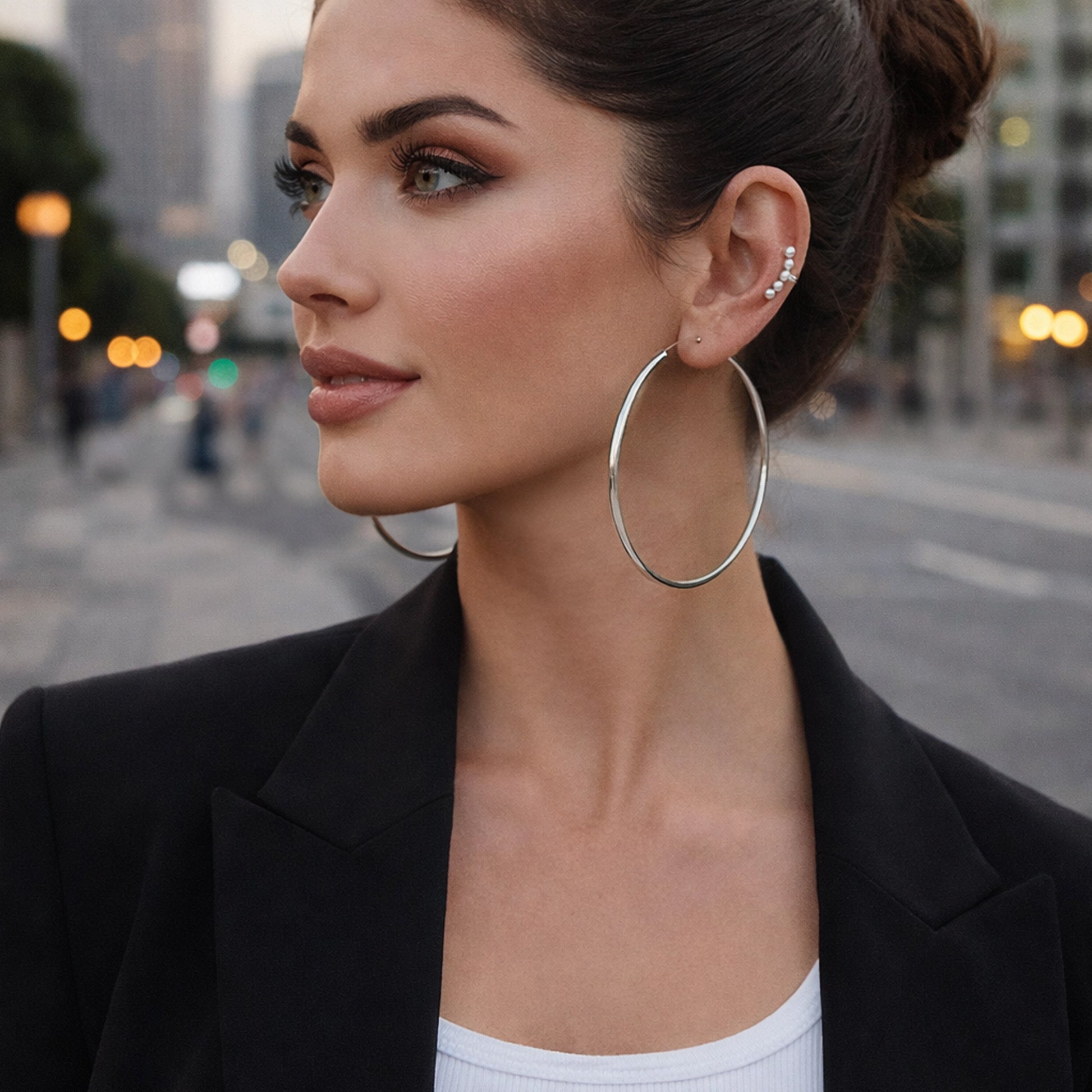 Beautiful stylish woman wearing a sterling silver dainty pearl ear cuff paired with large minimalist hoop earrings. Elegant modern ear stack featuring small delicate pearls along the ear cartilage, photographed in soft natural city lighting with a fashionable model and sleek urban background.