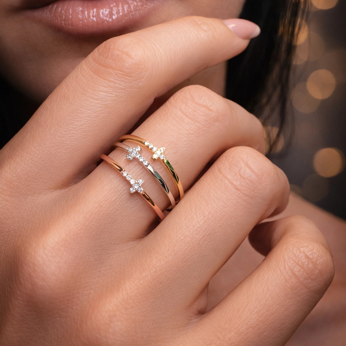 Sterling silver and gold cross stacking rings with CZ stones on woman’s hand, minimalist religious jewelry, delicate thin band rings, elegant Christian cross ring stack, close-up lifestyle jewelry photo.