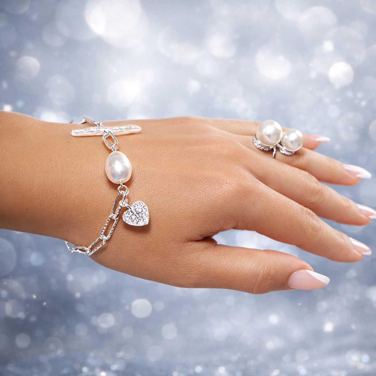 Close-up of a woman’s hand wearing a silver pearl bracelet with a heart charm and a double pearl ring, professionally retouched with smooth natural skin, elegant manicure, sparkling stones, and a soft light studio background.