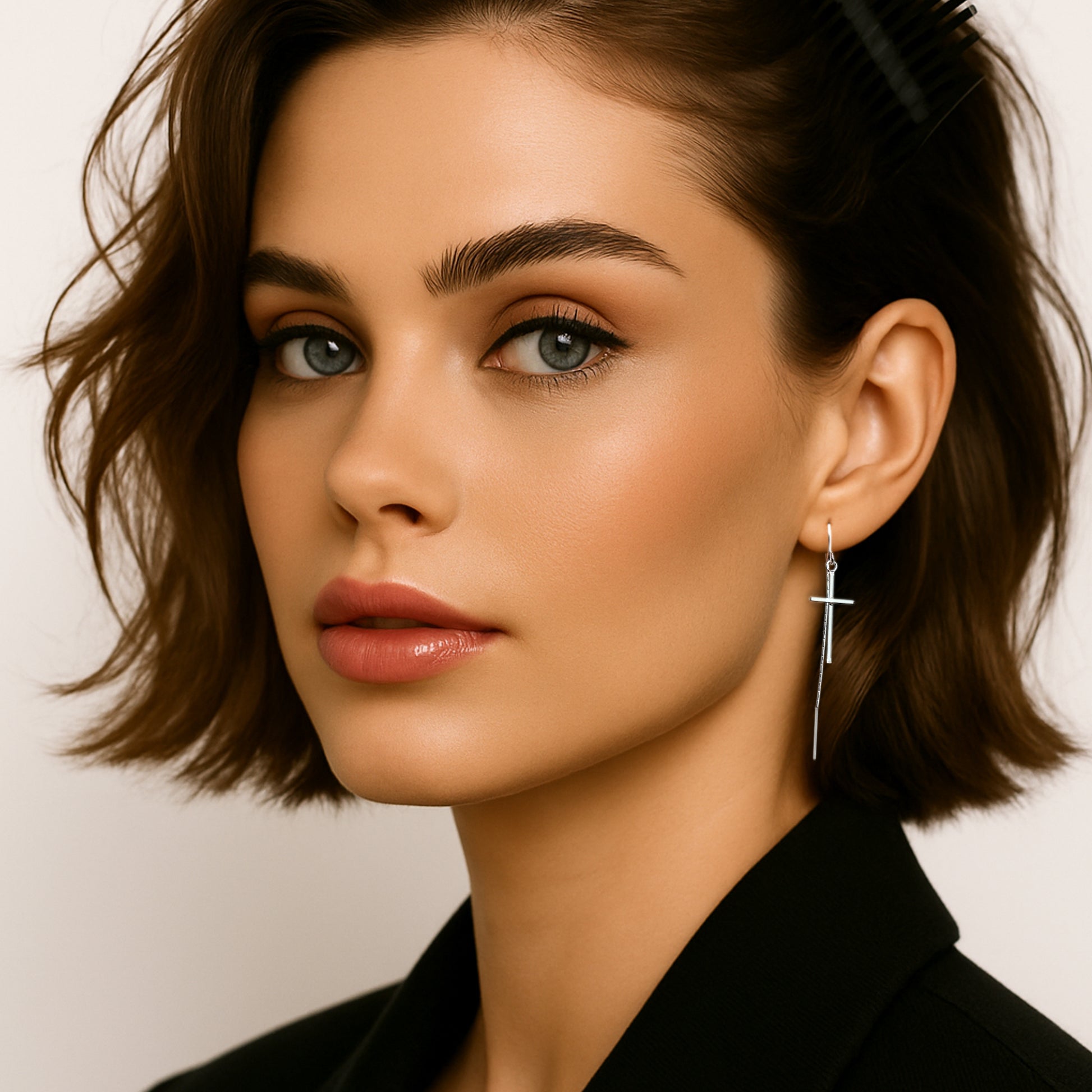 Elegant woman wearing sleek sterling silver cross threader earrings, styled with a black outfit and softly waved short hair pinned to the side.
