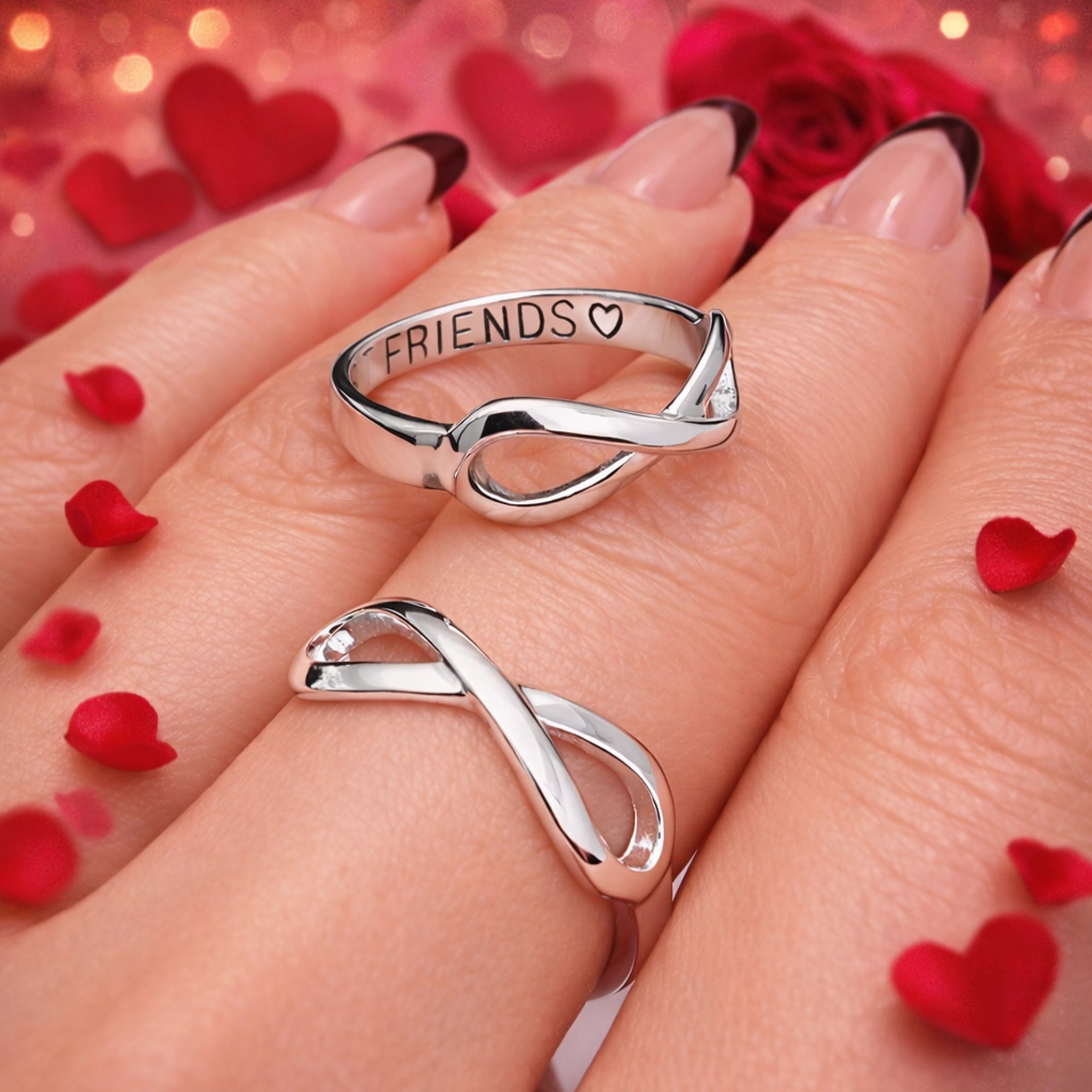 Silver 'FRIENDS' heart ring on a hand with red heart-shaped petals and roses in the background