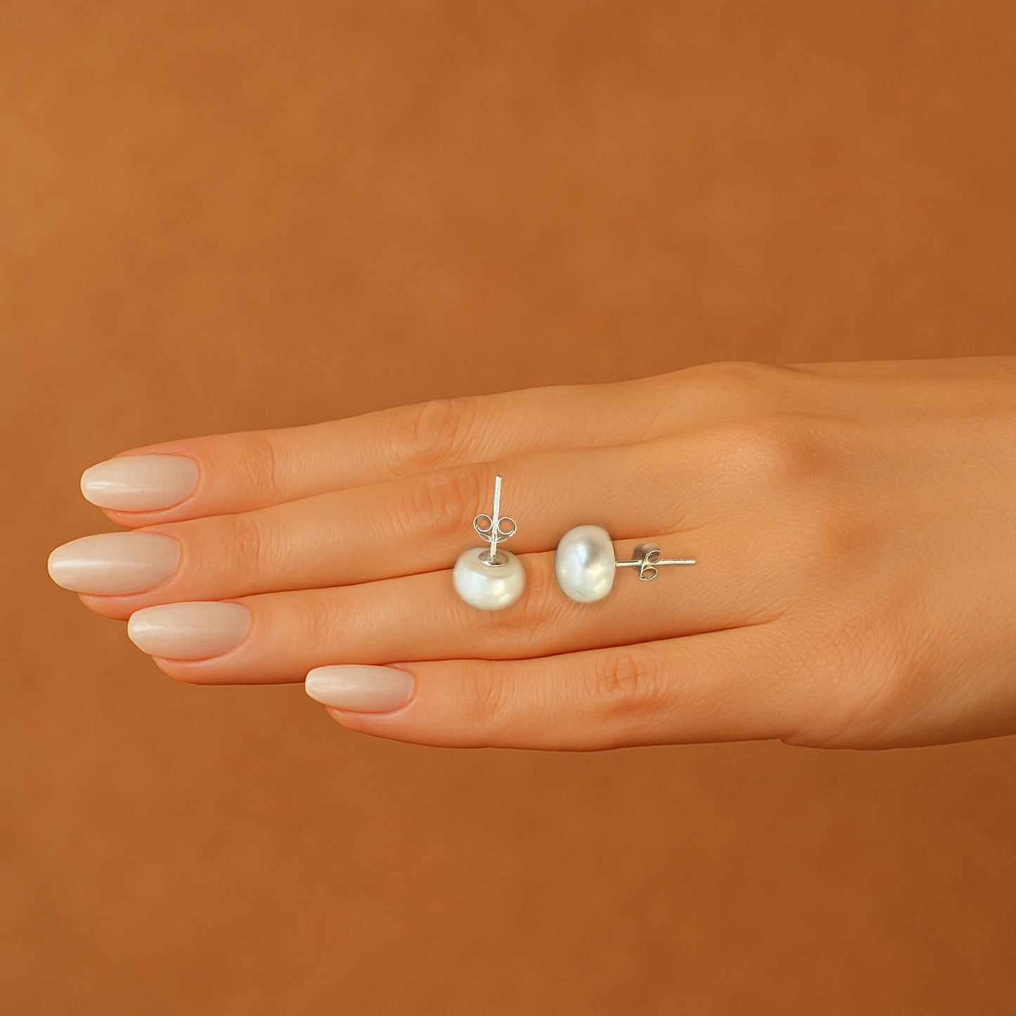 Sterling silver white pearl stud earrings with natural luster resting on manicured hand with neutral nails.