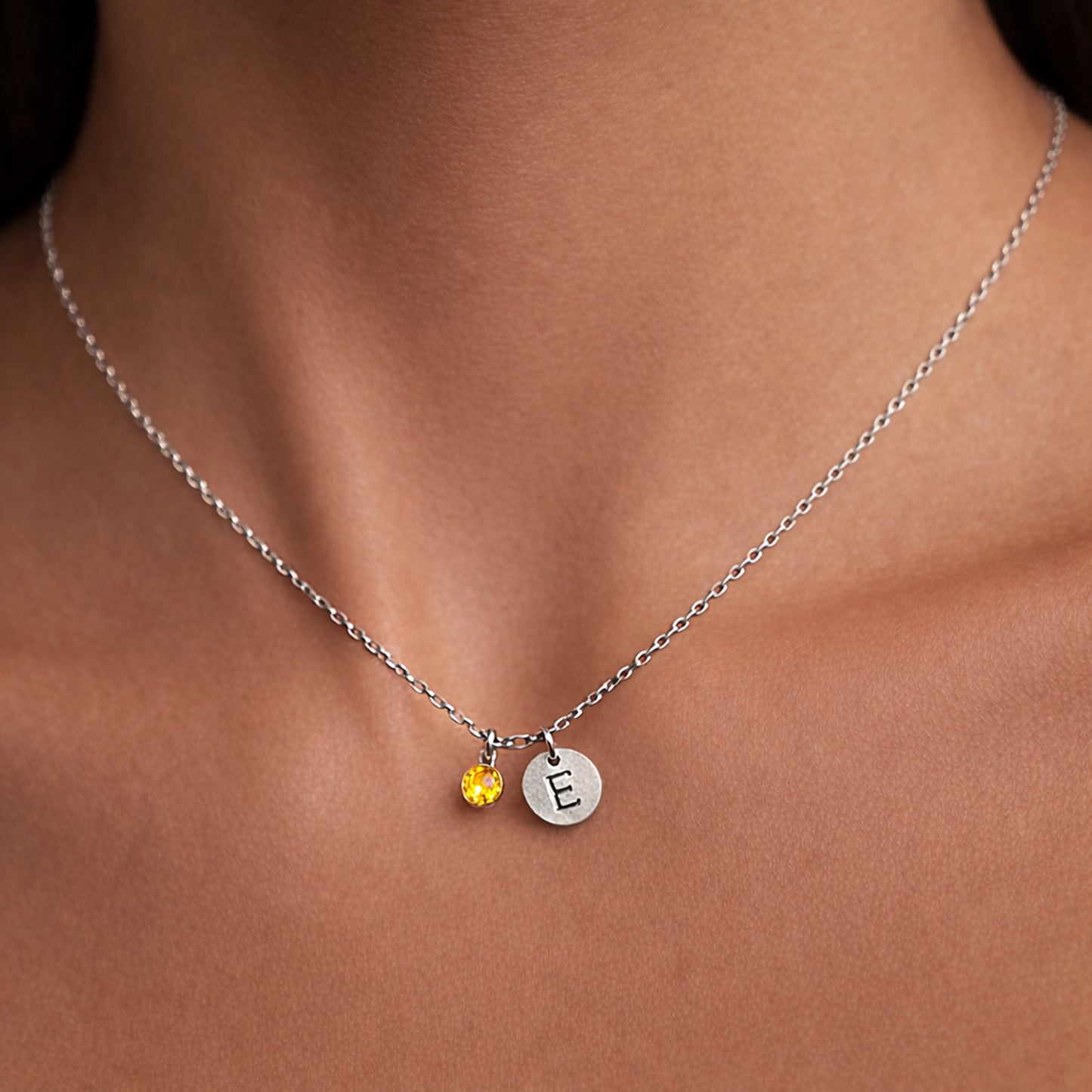 Sterling silver initial necklace with petite yellow tourmaline bezel charm and engraved letter disc, delicate thin chain, close-up on smooth neck, studio lighting, minimalist fine jewelry detail